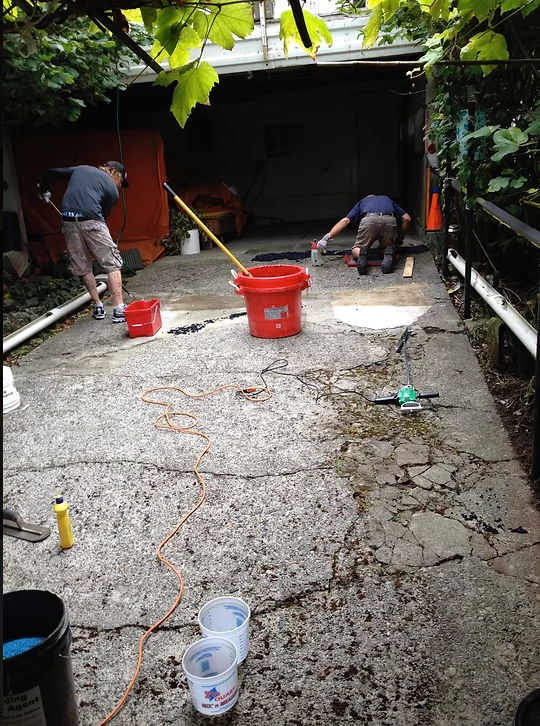 Two men are working on a concrete driveway with buckets and a mop