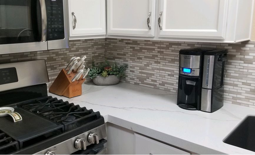 A kitchen with a stove , microwave , coffee maker and sink.