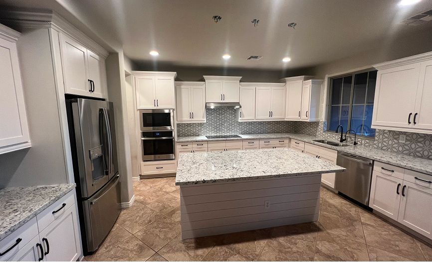 A kitchen with white cabinets , granite counter tops , stainless steel appliances and a large island.