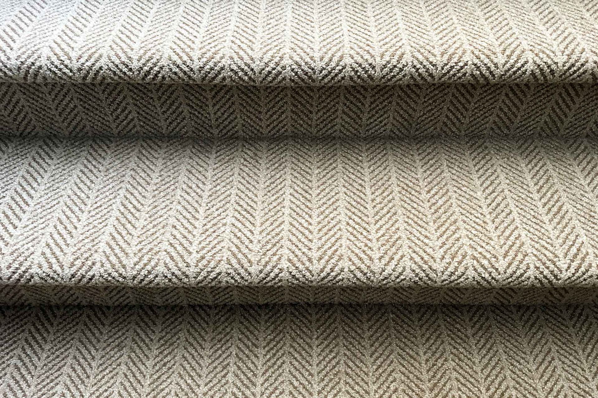 A close up of a carpeted staircase with a herringbone pattern.