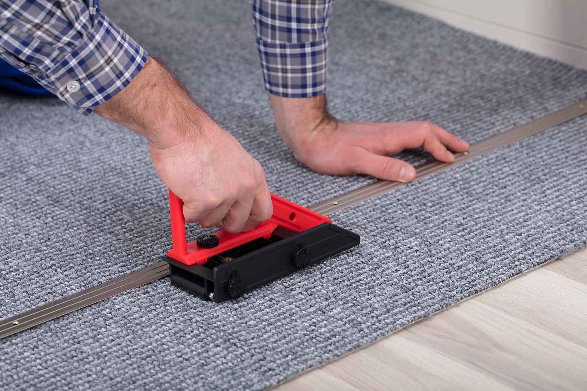 A man is cutting a piece of carpet with a tool.