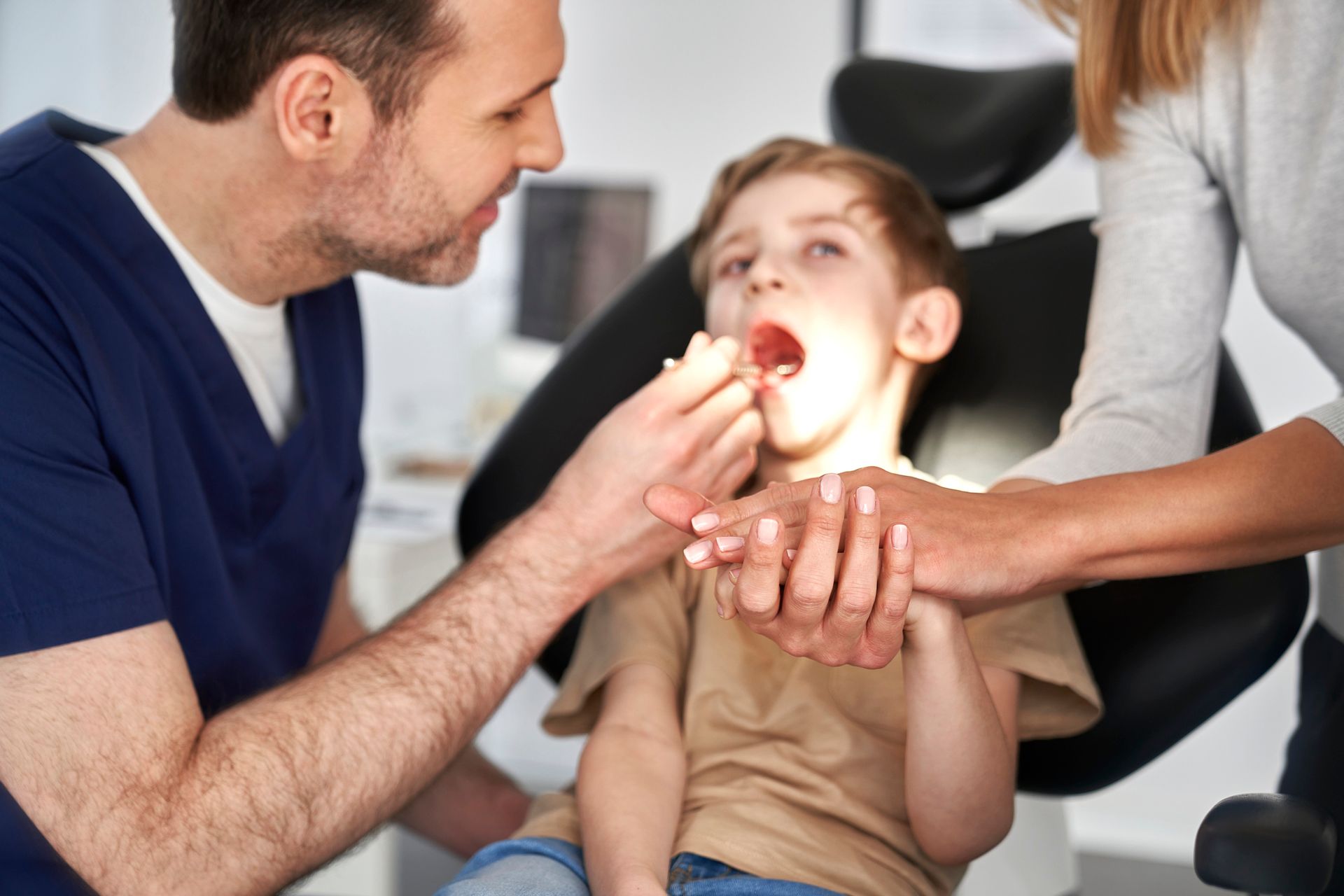 Dentist examining a young boy's mouth; the boy is in a chair with his mouth open.
