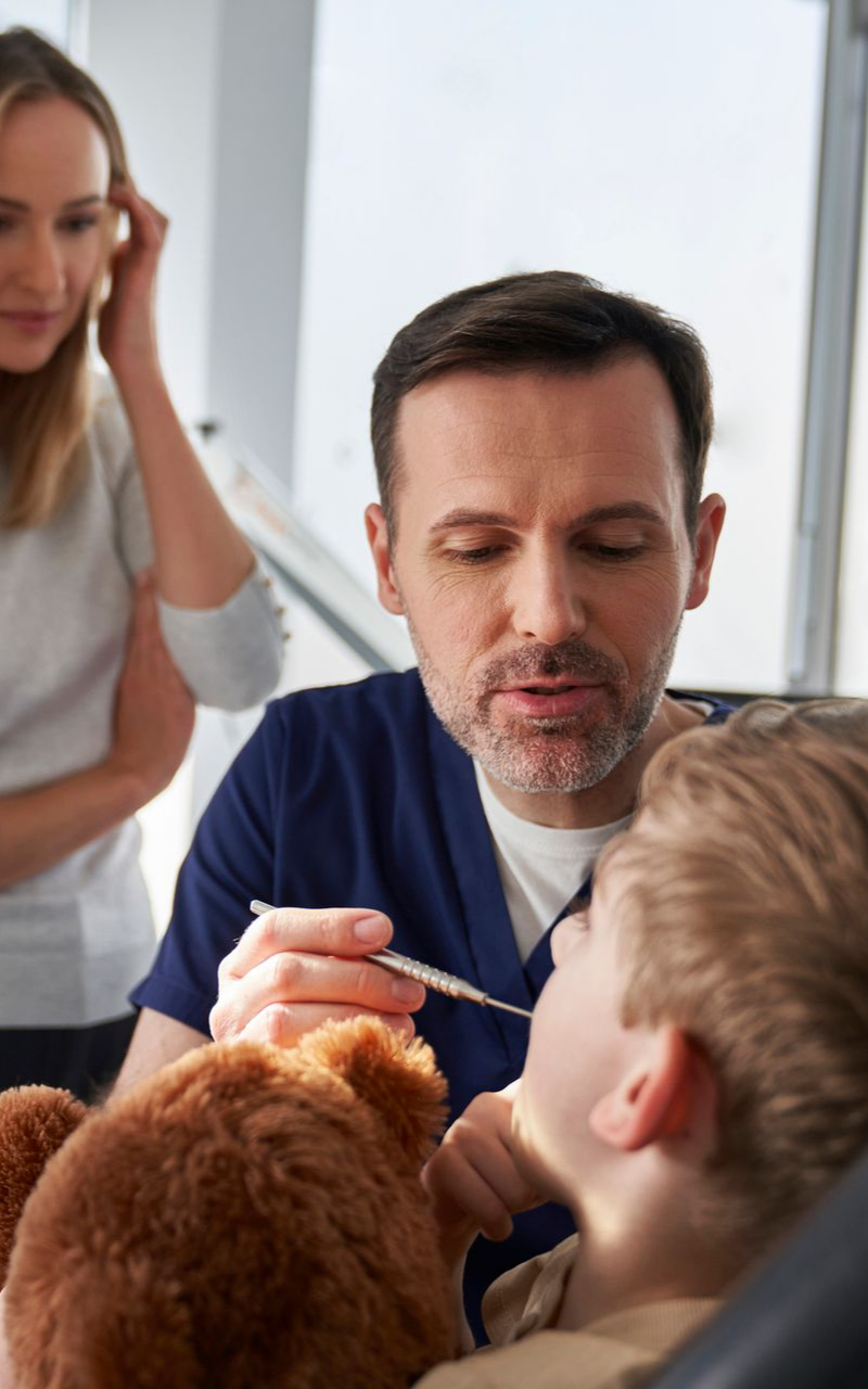 Little boy holding a teddy bear, while visiting a family dentist with his mother.
