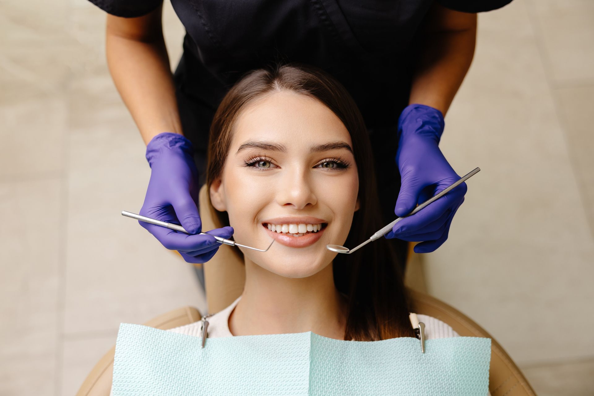 A happy patient is examined by a gloved, unidentified doctor for cosmetic dentist services.