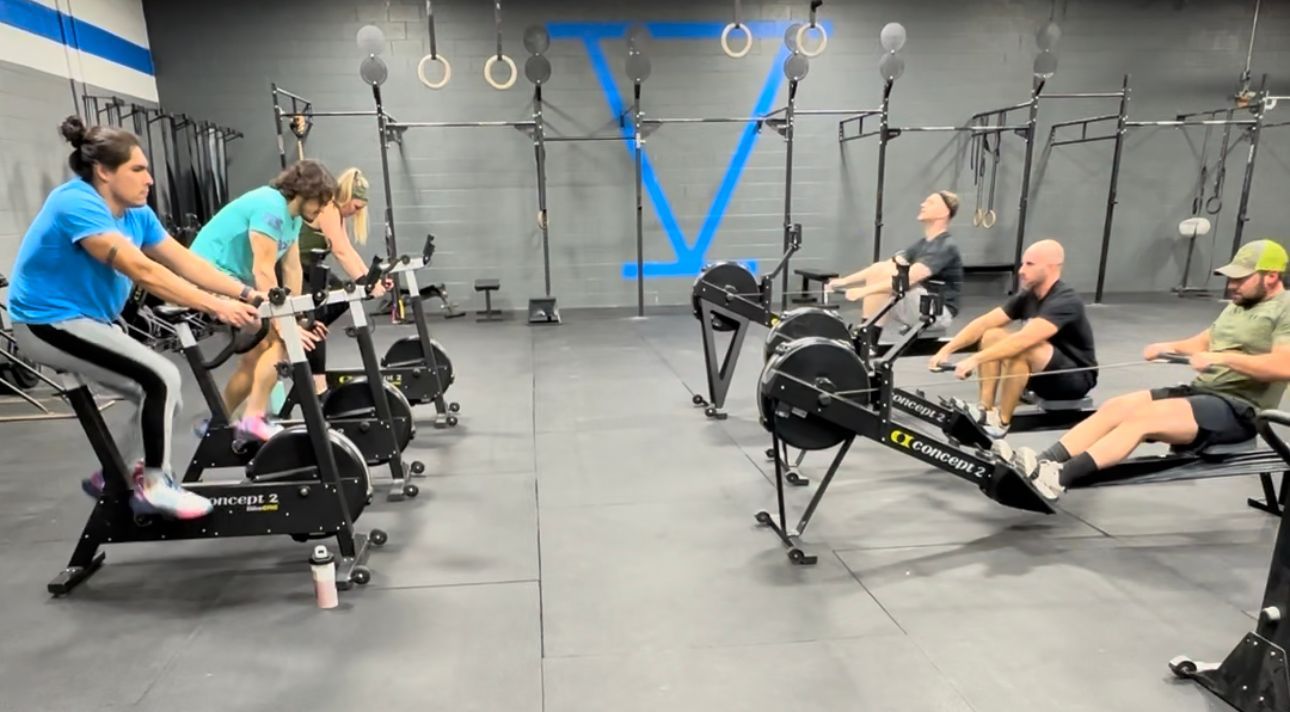 A group of people are riding exercise bikes and rowing in a gym.