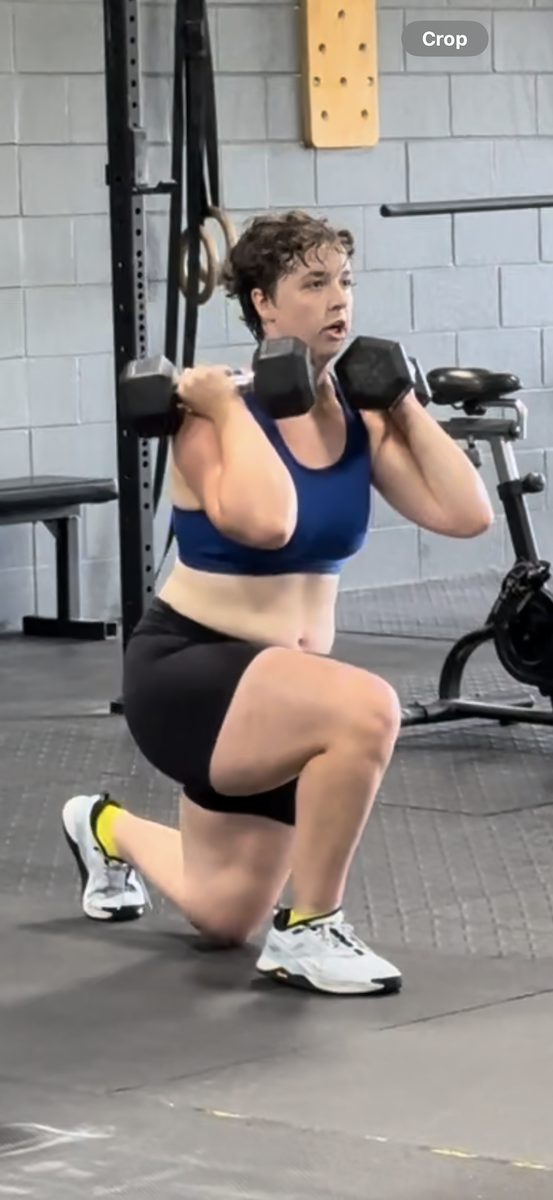 A woman is squatting with dumbbells on her shoulders in a gym.