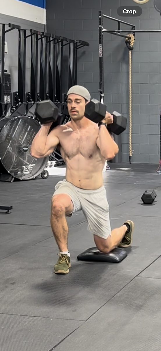 A shirtless man is doing lunges with dumbbells in a gym.