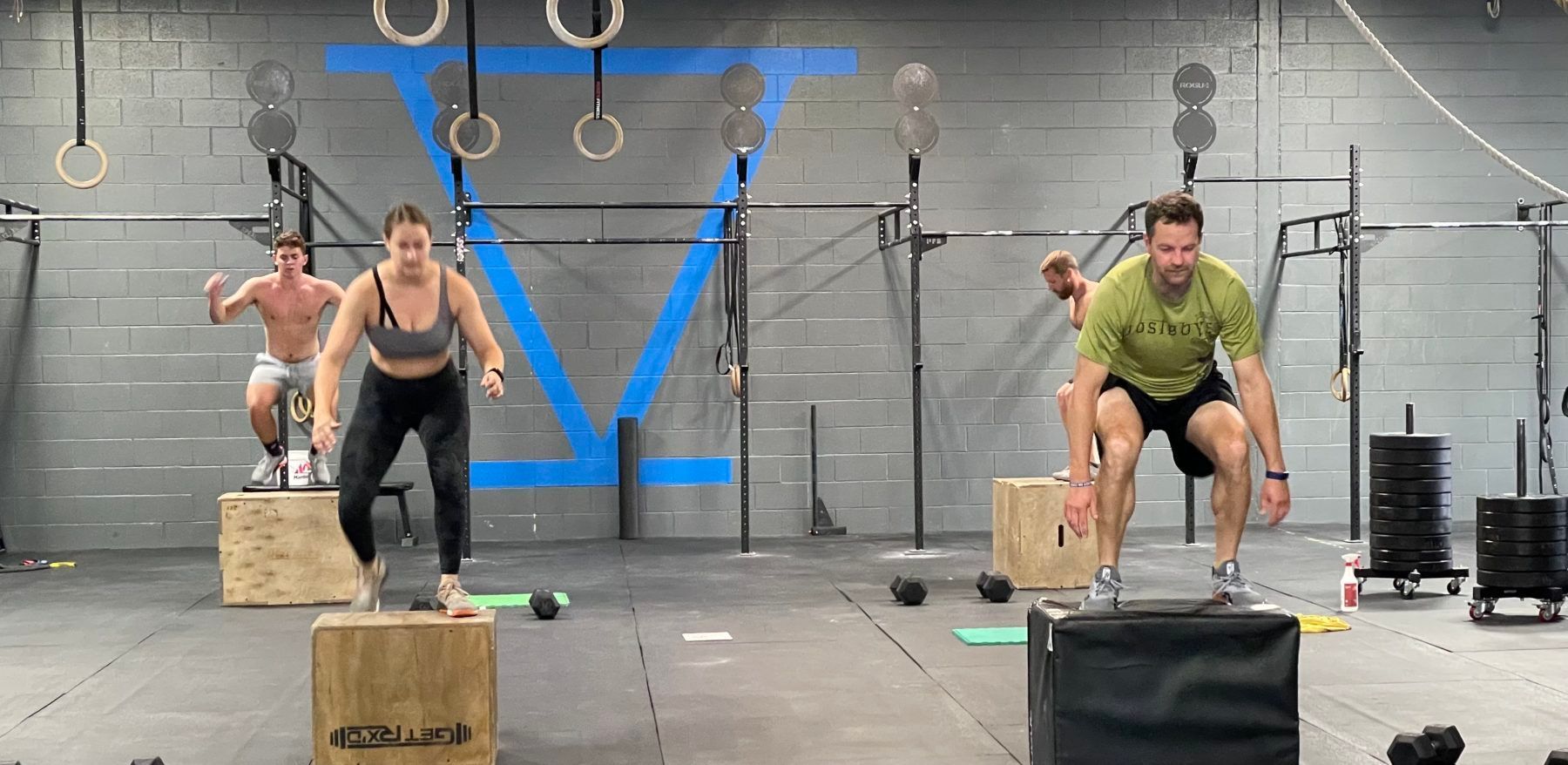 A group of people are jumping over wooden boxes in a gym.