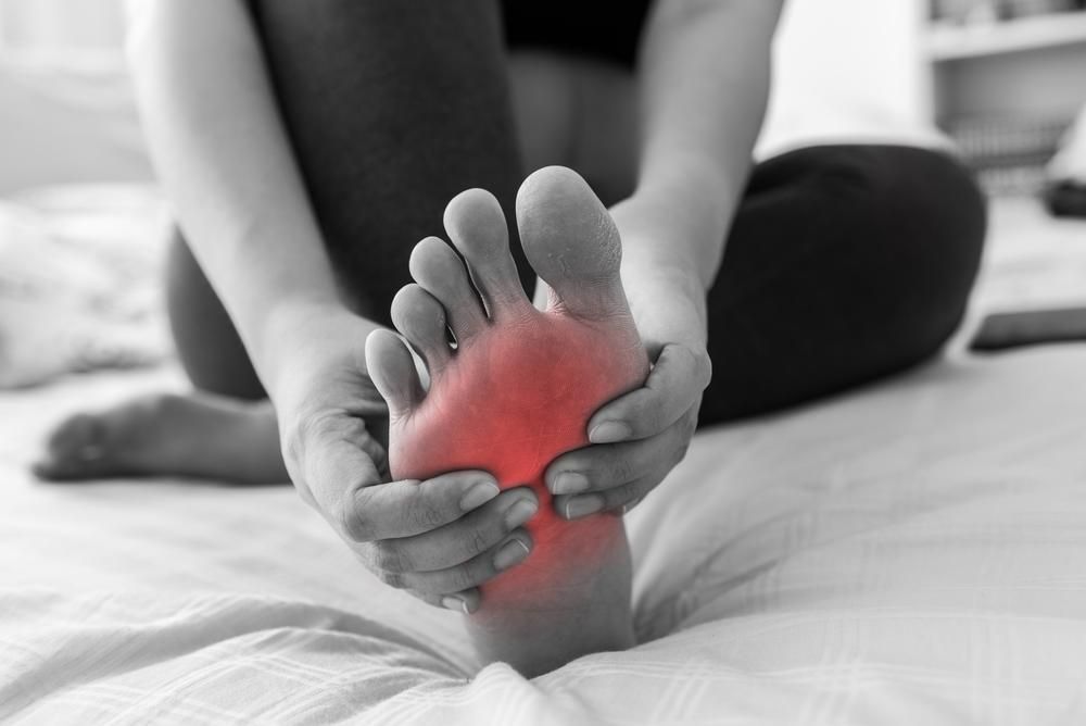 A Woman Is Sitting on A Bed Holding Her Foot in Pain — Betta Foot Clinic in Calamvale, QLD