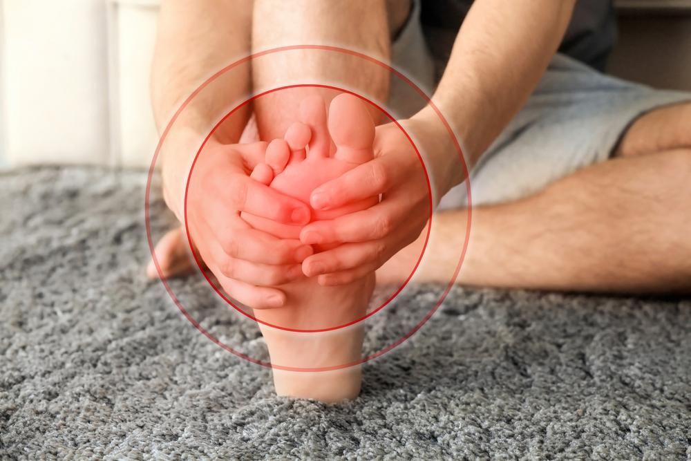 A Person Is Sitting on The Floor Holding Their Foot in Pain — Betta Foot Clinic in Calamvale, QLD