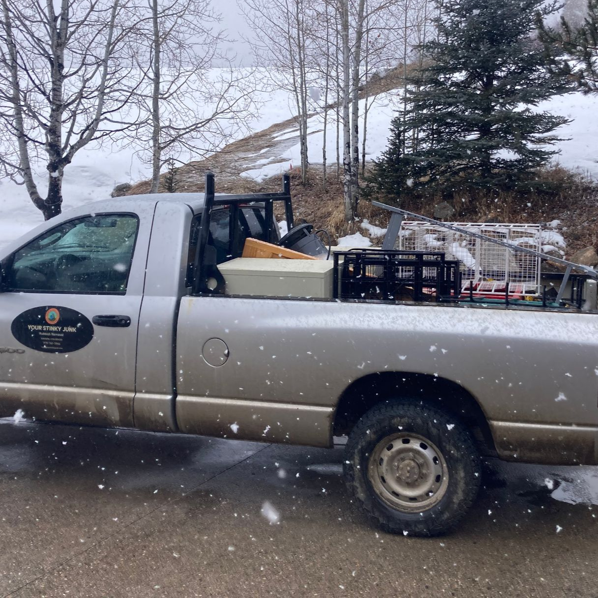 Silver pickup truck parked in snow, carrying equipment racks and tools in the truck bed, with trees in the background.