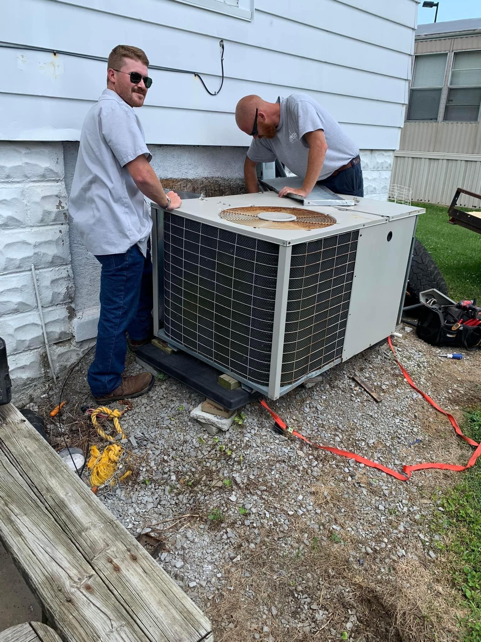 Two technicians servicing an outdoor HVAC unit beside a house