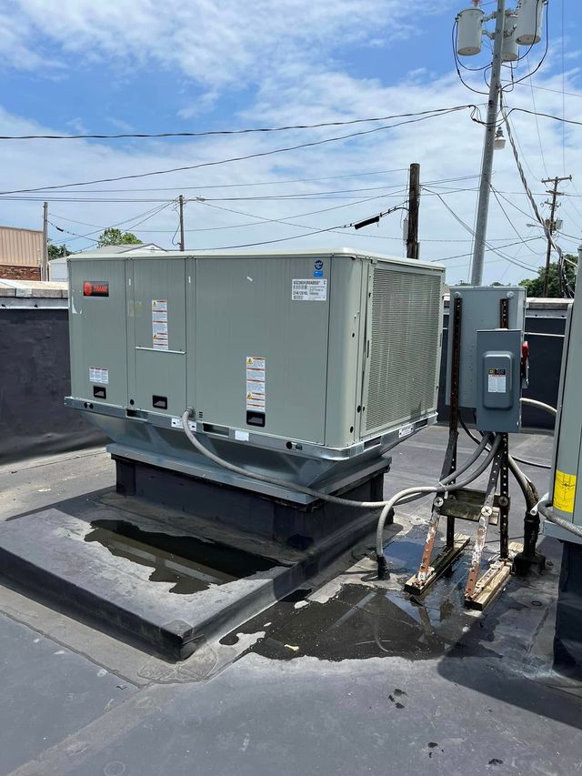Gray rooftop HVAC unit on a raised platform, with utility poles and wires in the background.