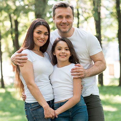 A man , woman and child are posing for a picture in a park.