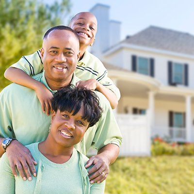 A man is carrying a child on his shoulders in front of a house.