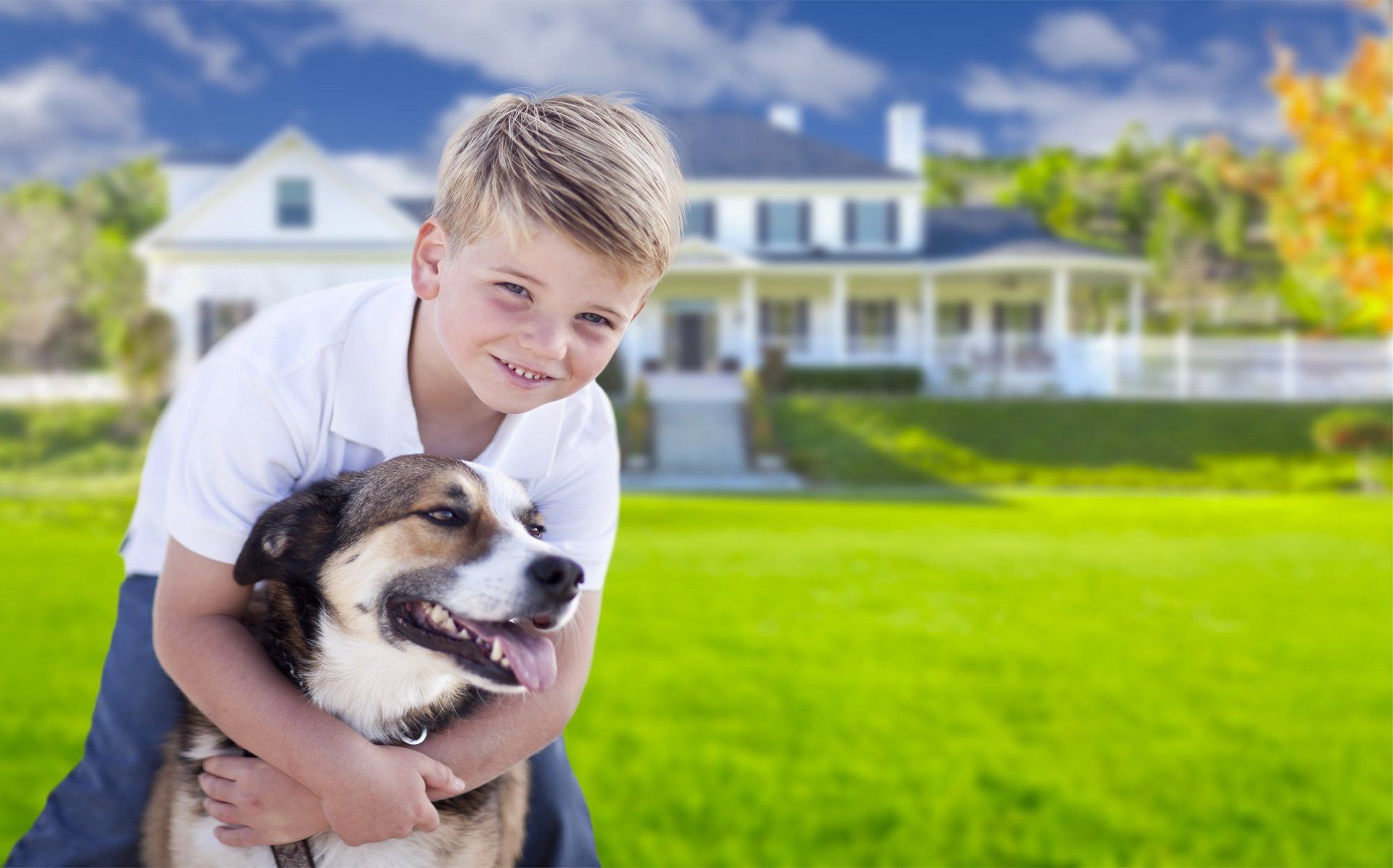 A young boy is holding a dog in front of a house.