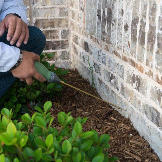 A man is kneeling down next to a brick wall holding a hose