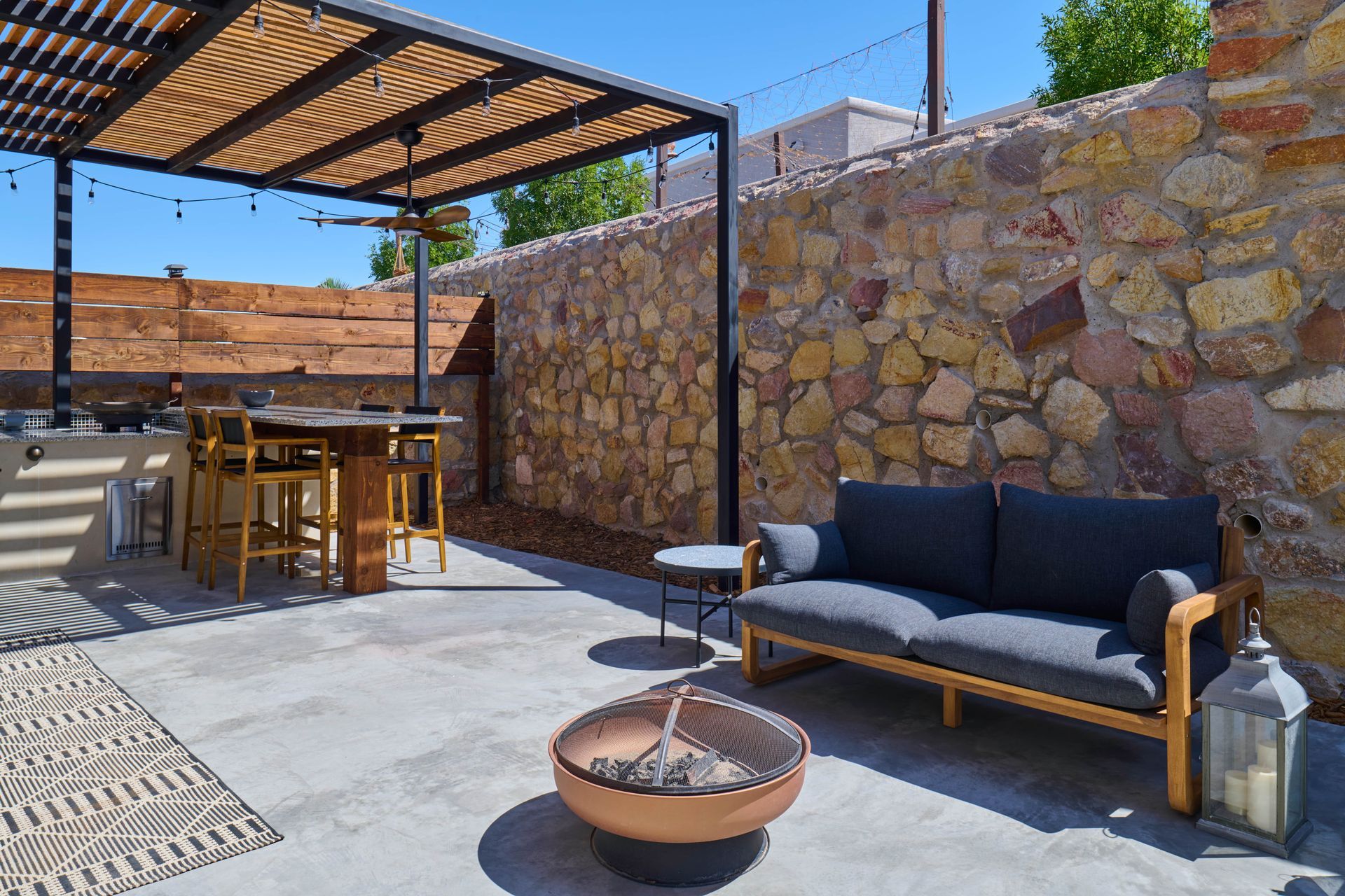 Patio with pergola, stone wall, sofa, fire pit, and bar seating.