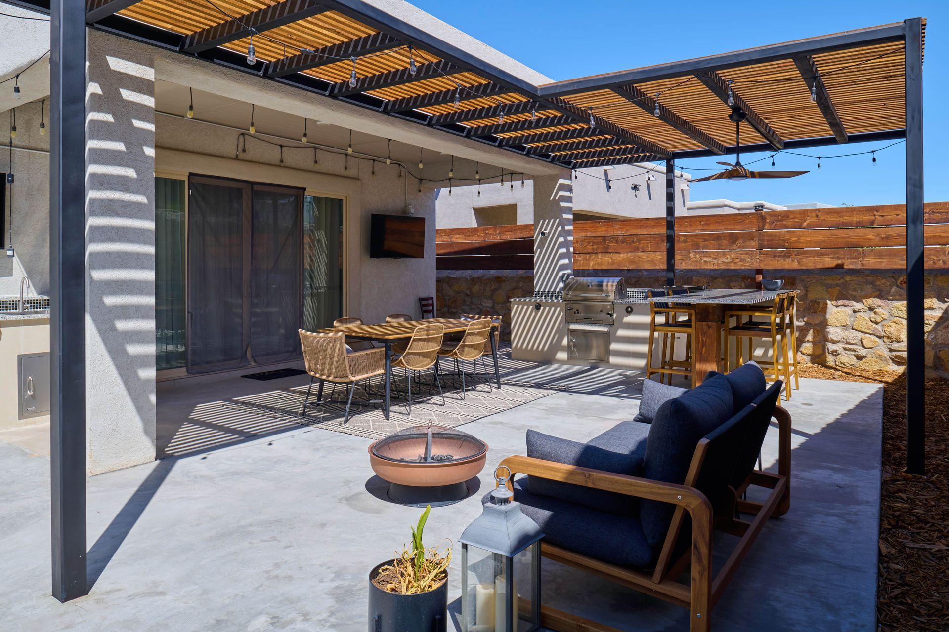 Patio with pergola, outdoor furniture, dining table, and fire pit under a clear blue sky.