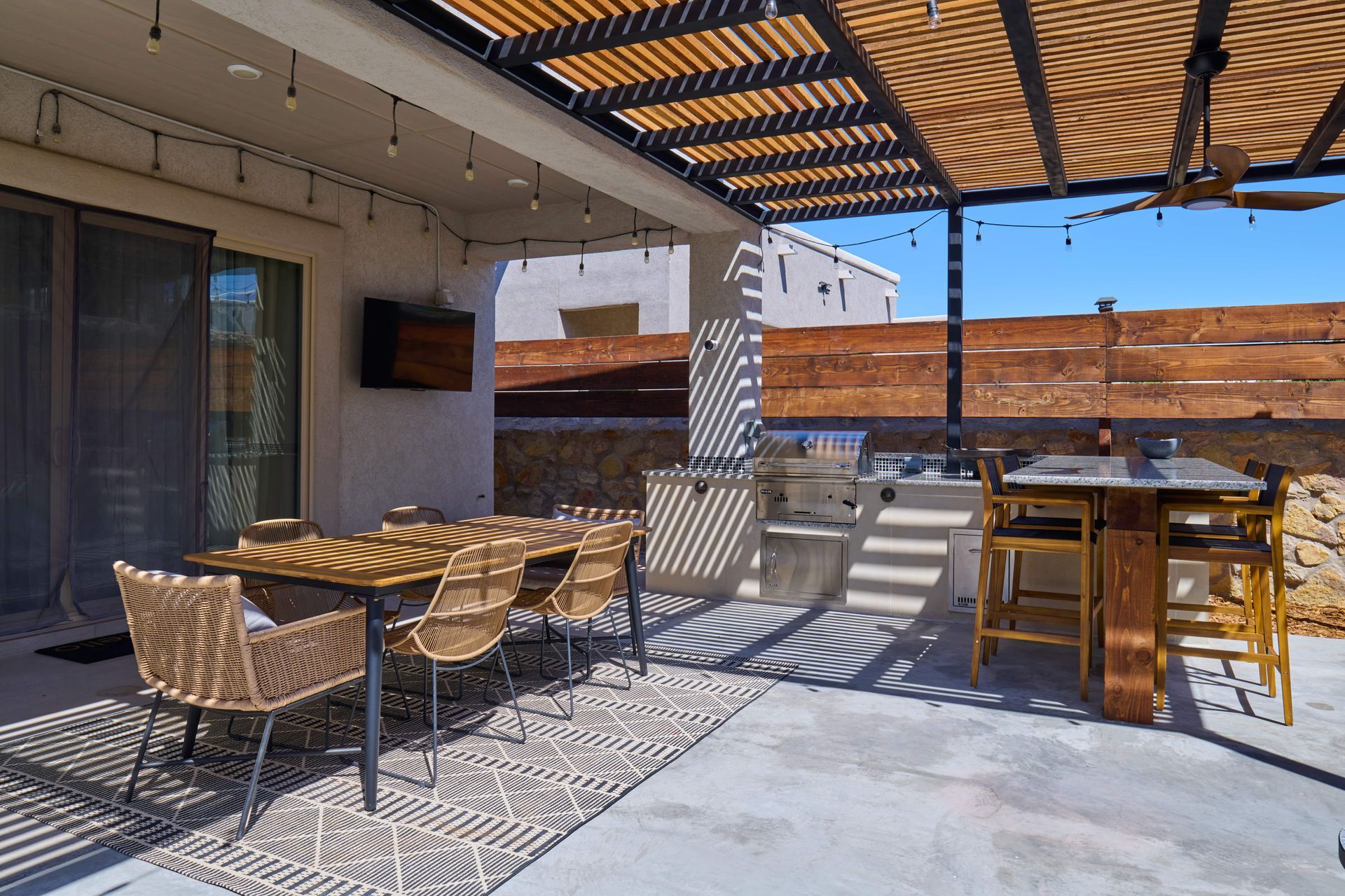 Outdoor patio with dining area, kitchen, and bar under a pergola.
