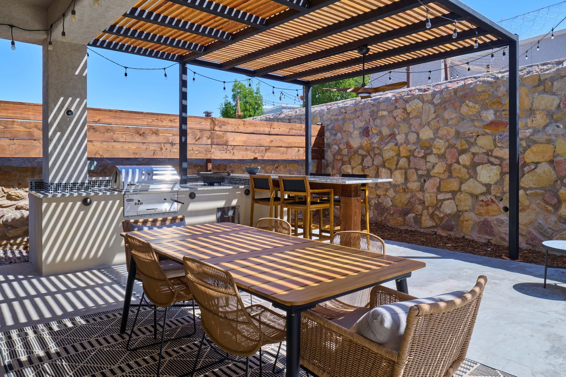 Outdoor patio with dining table, chairs, grill, and bar under a wooden pergola.