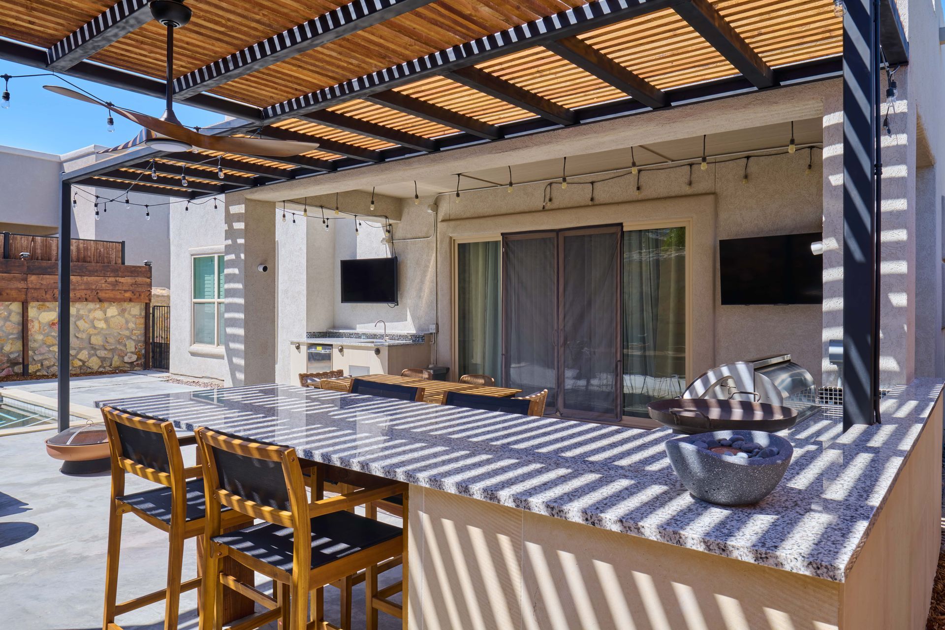 Outdoor patio with overhead pergola, bar, stools, and built-in grill.