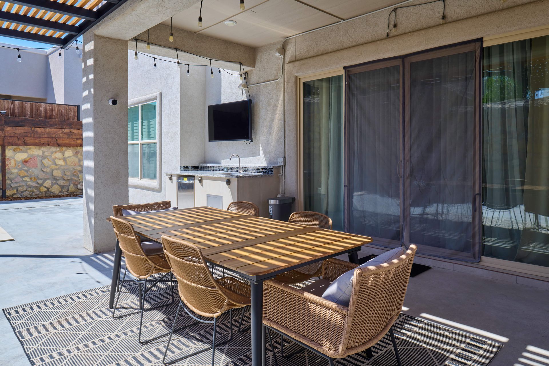 Patio with dining table and chairs, outdoor kitchen, TV, and string lights.