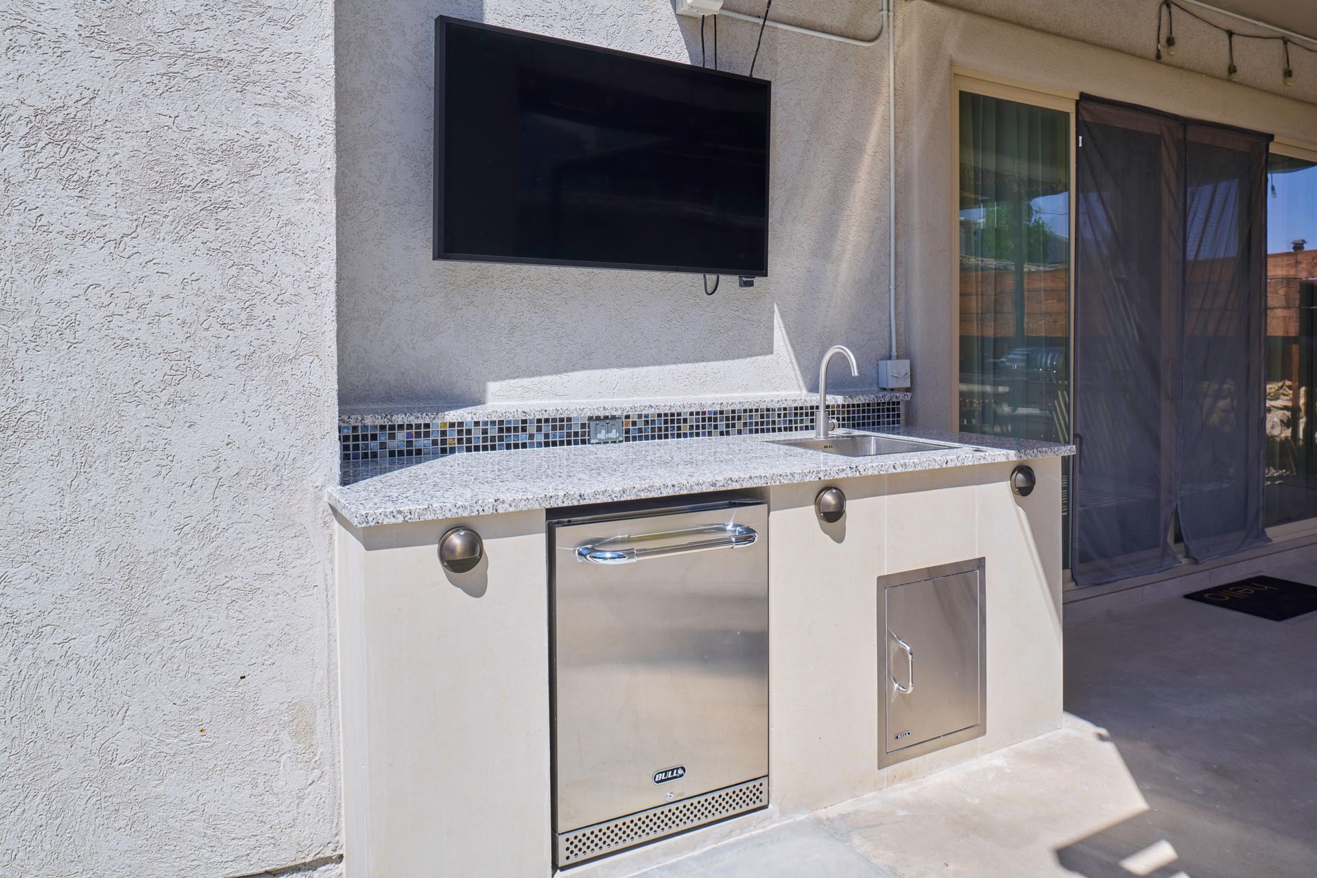 Outdoor kitchen with TV, stainless steel appliances, and granite countertop.