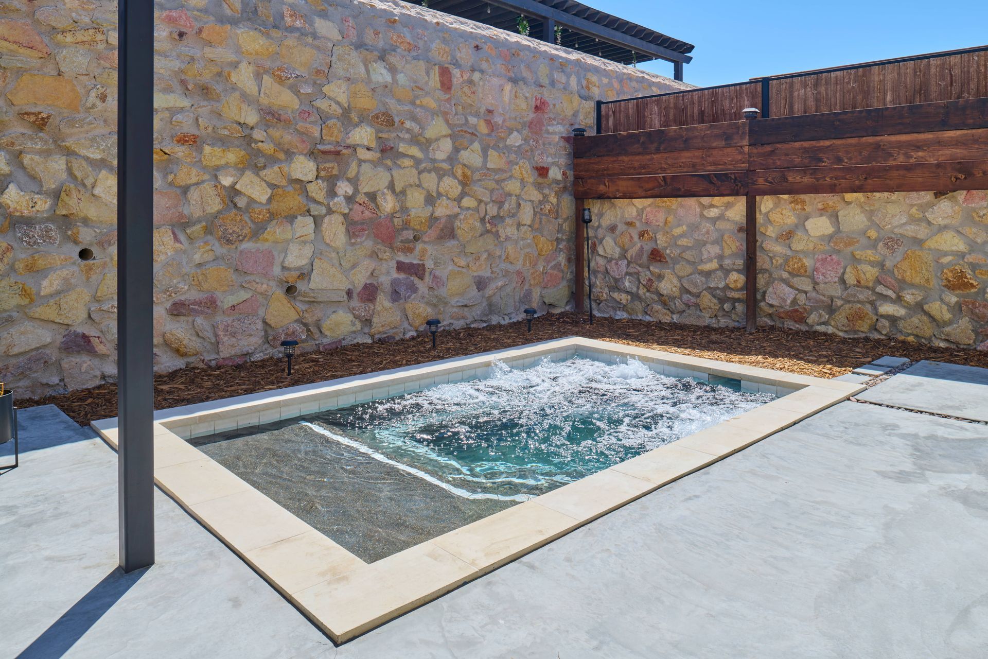 Small outdoor spa enclosed by stone wall and wooden fence.