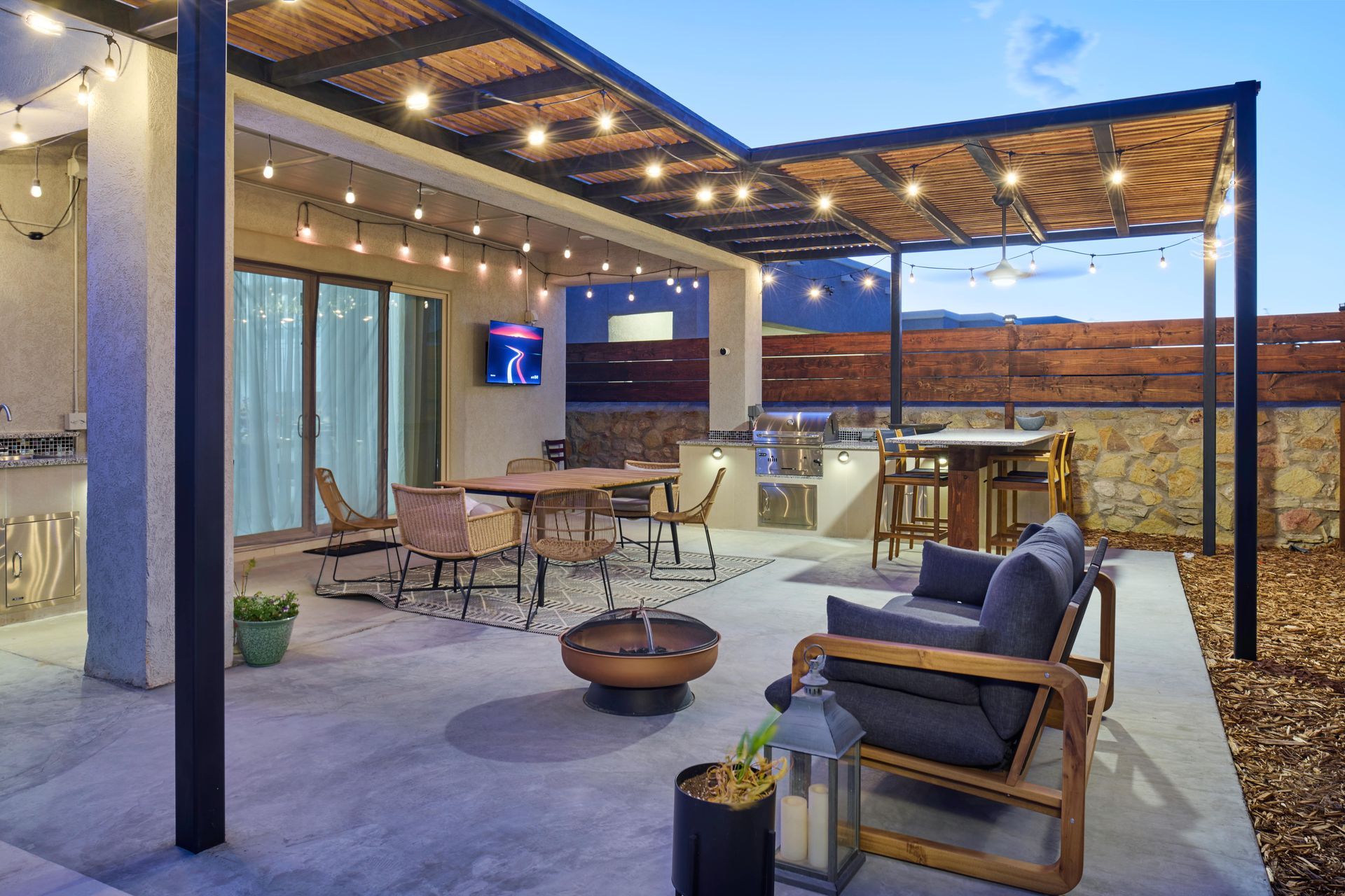 Outdoor patio with seating, dining table, built-in kitchen, and string lights at dusk.