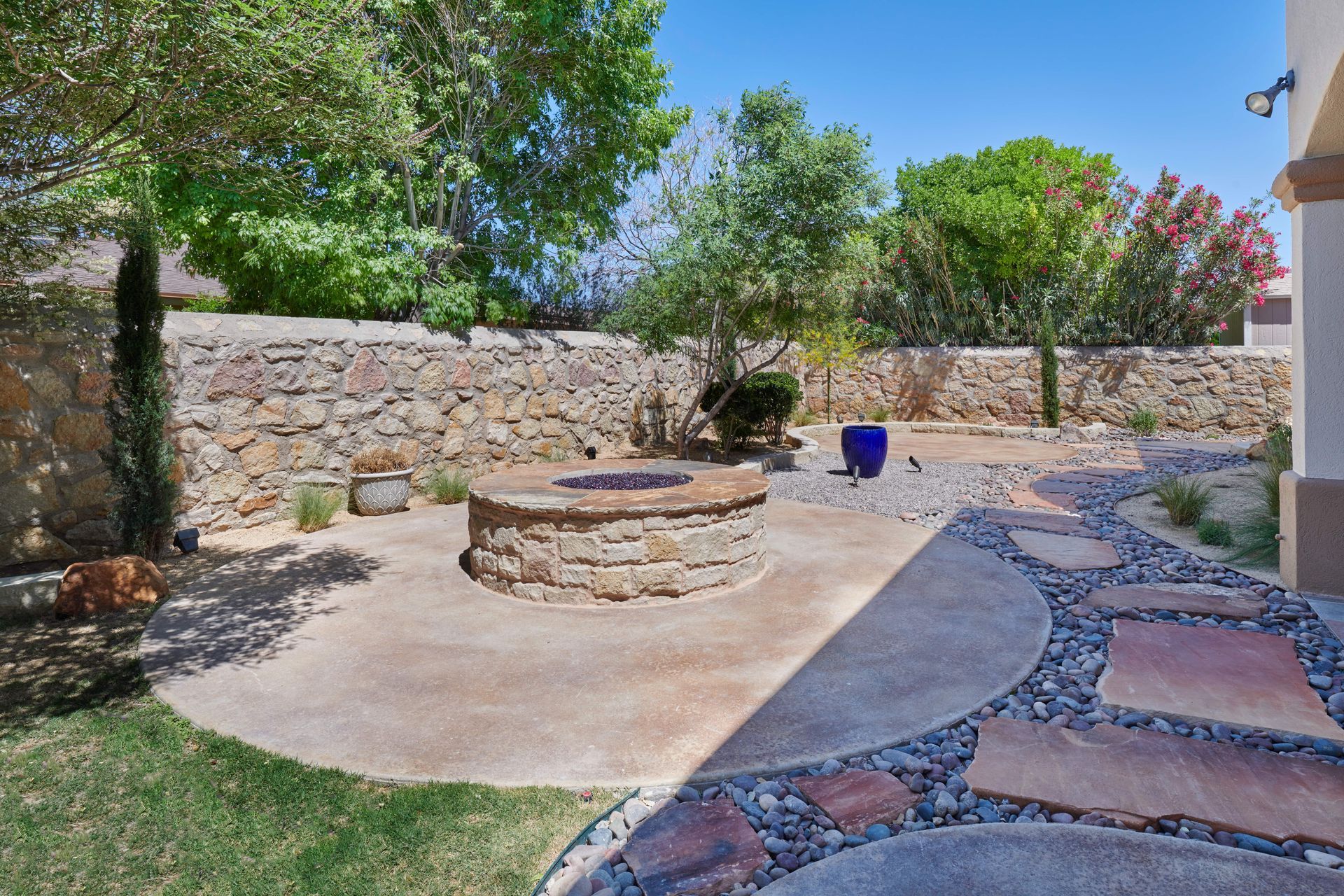 Stone fire pit in a backyard with a stone wall and landscaping.