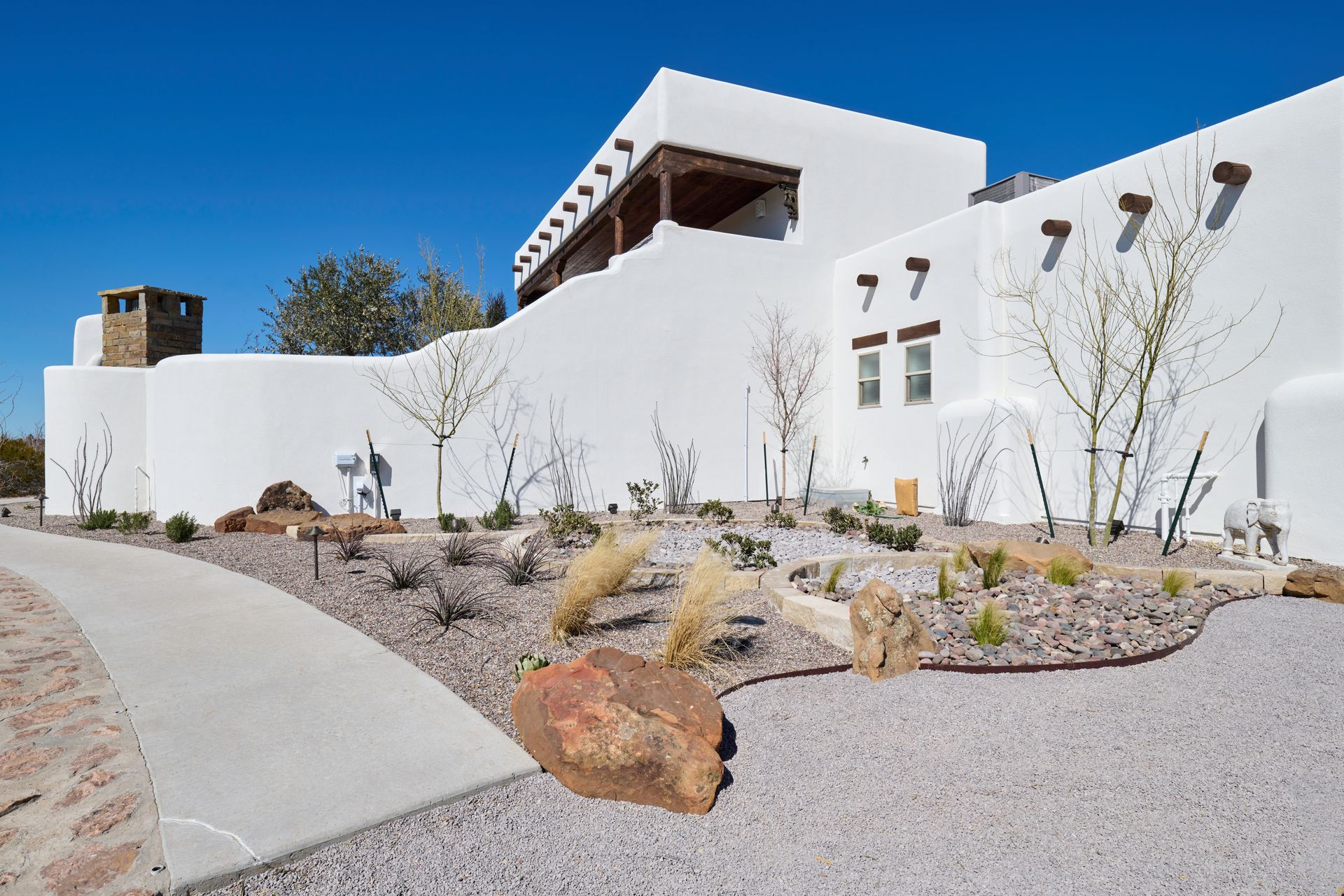 White adobe building with a walkway, gravel landscaping, and clear blue sky.