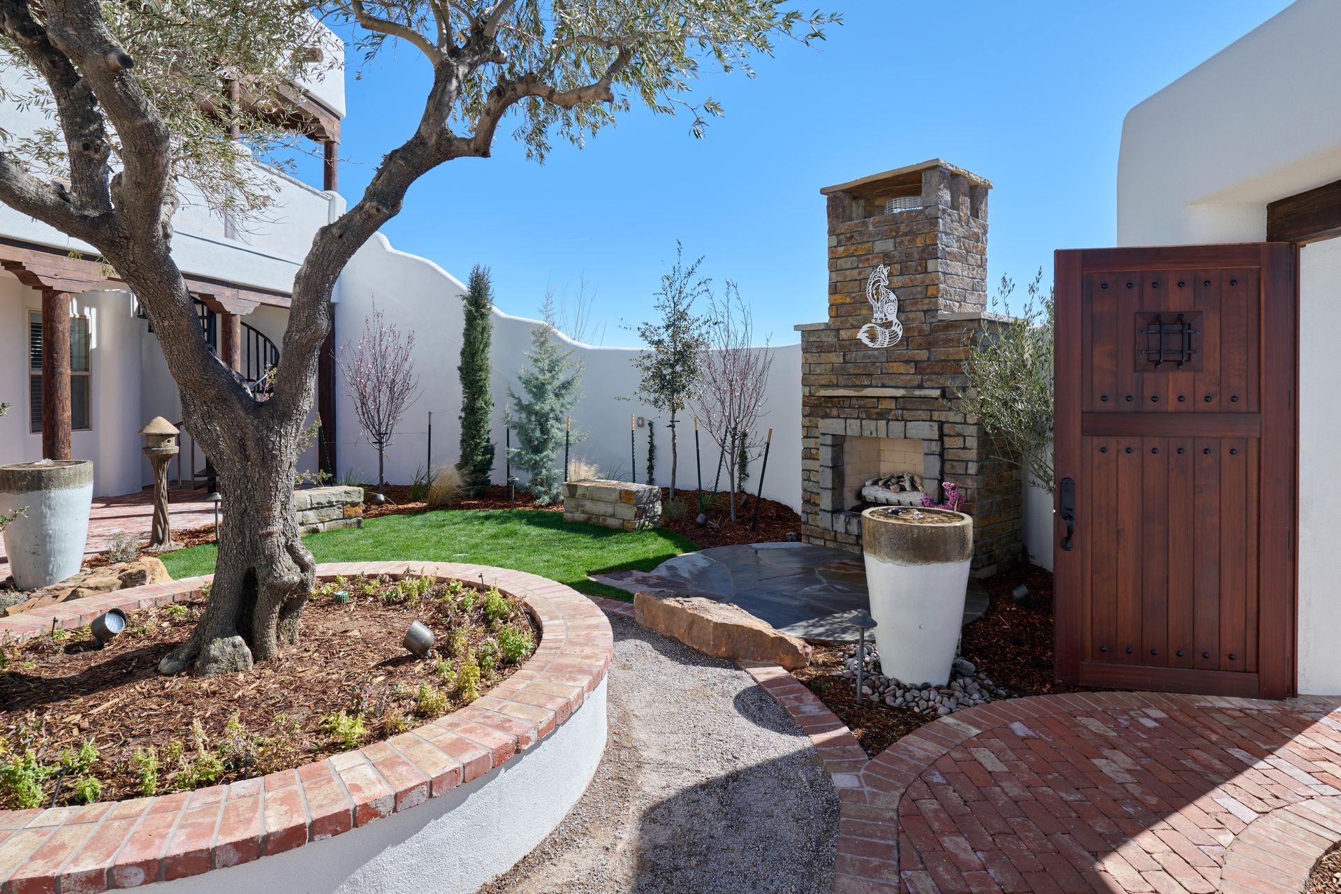 Courtyard with brick pathways, a stone fireplace, and a wooden gate.