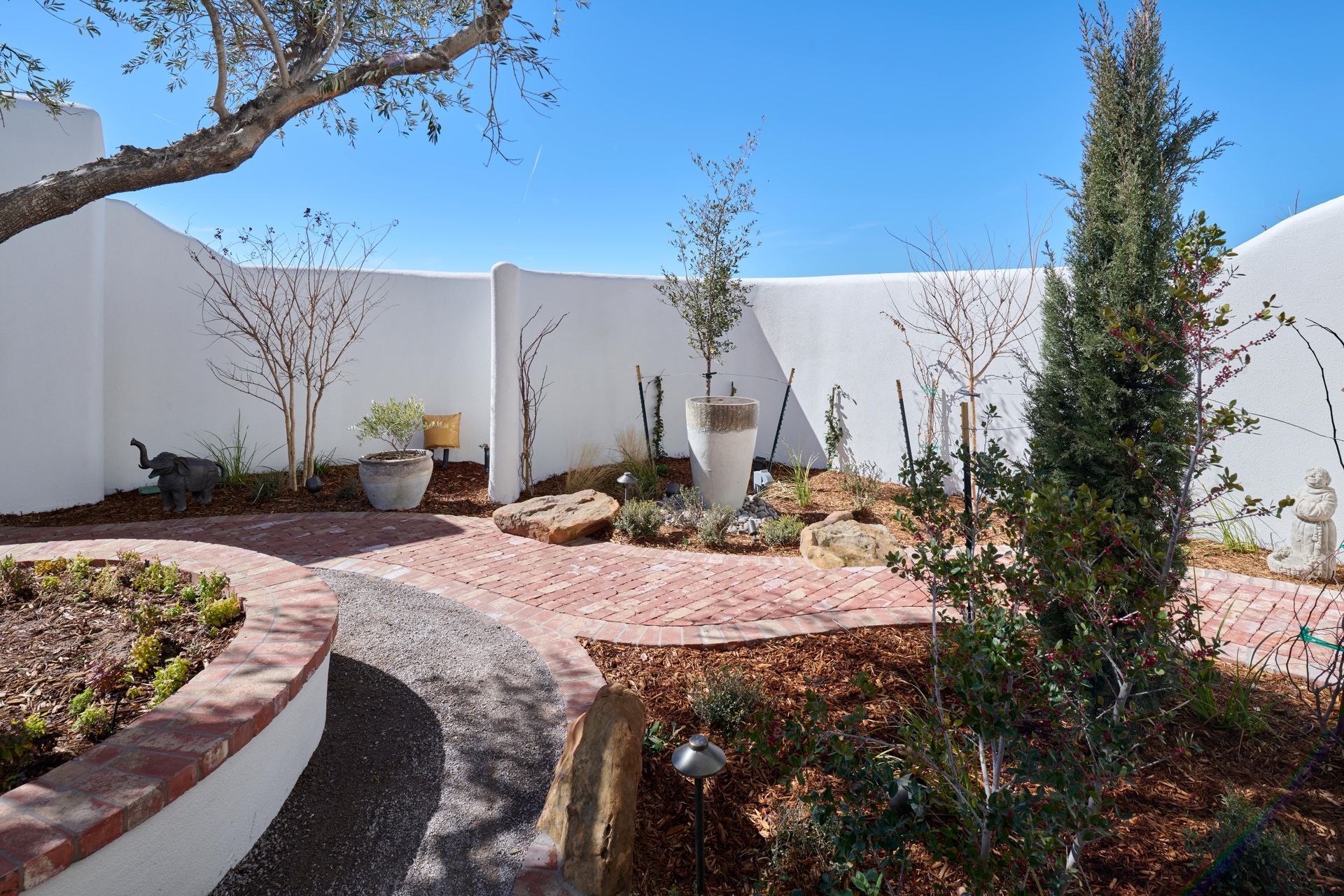 Outdoor garden with curved brick pathways, stone beds, and white stucco walls.