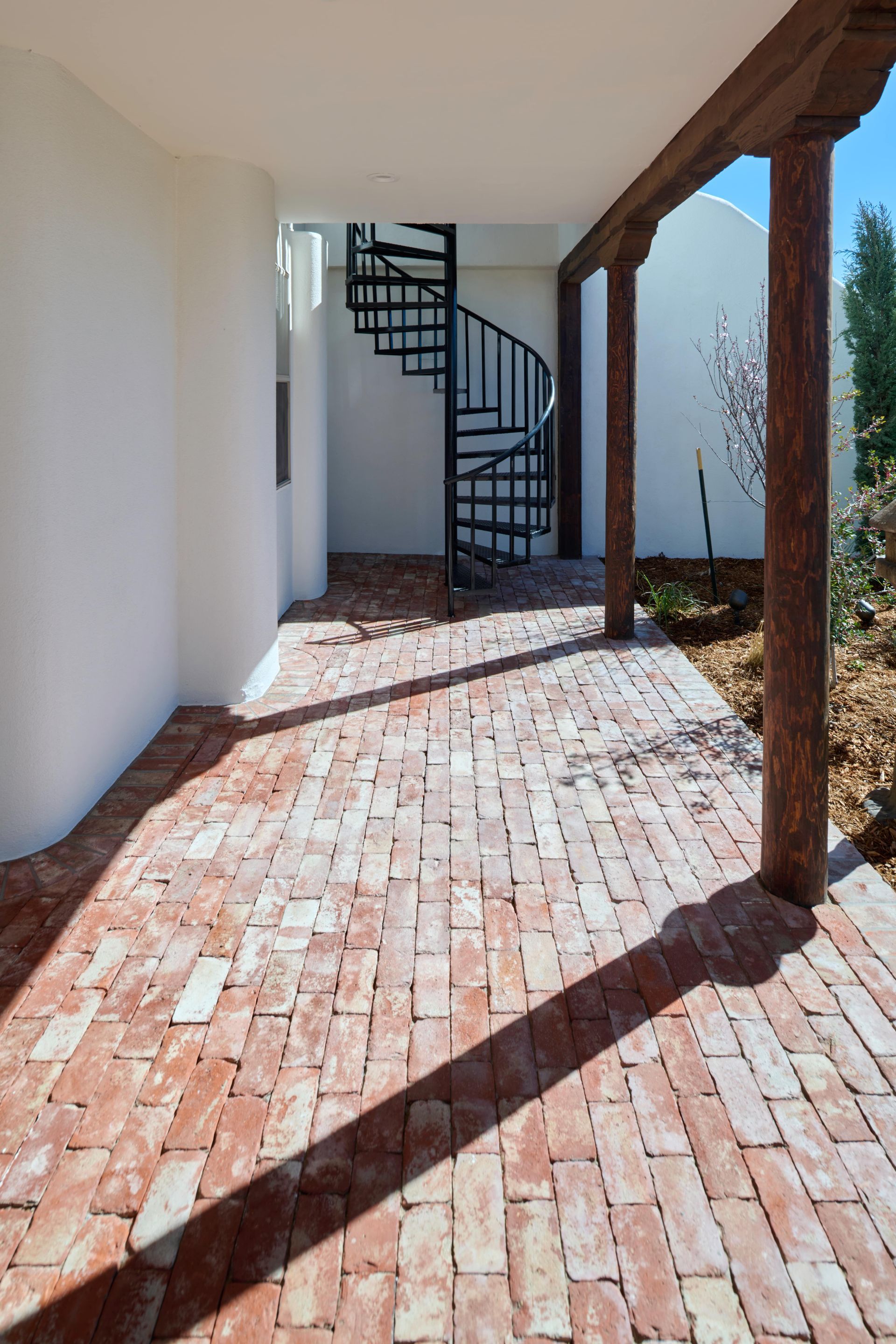 Brick walkway with spiral staircase, white walls, and wooden beams.