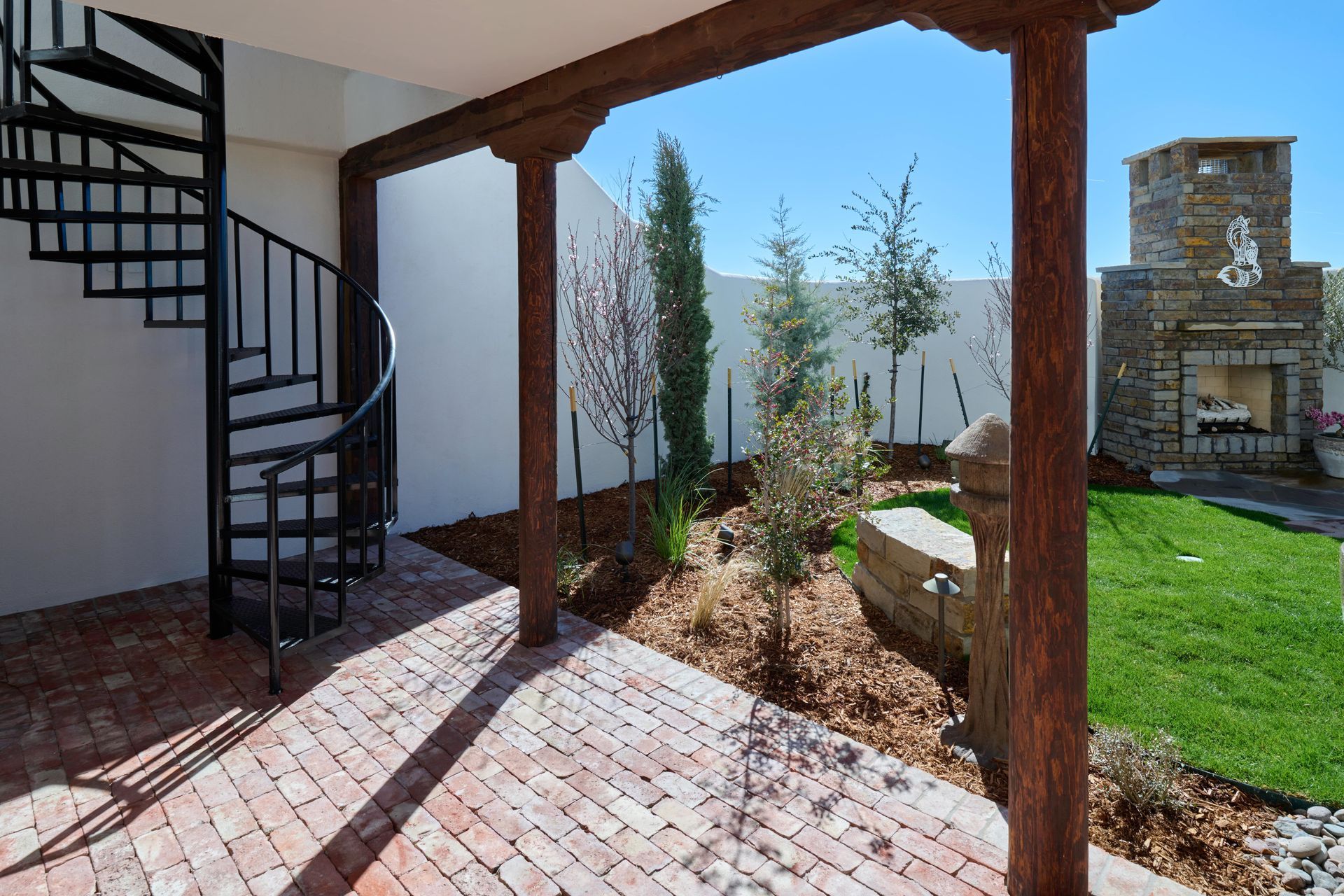 Brick patio with spiral staircase, view to courtyard with fireplace and trees.