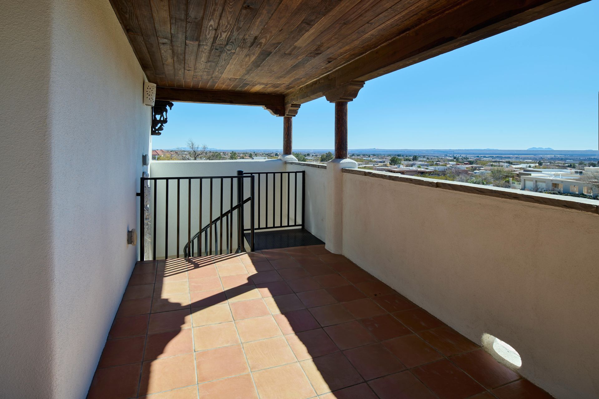 Terrace with terracotta tiles, black railing, and city view under a wooden beam ceiling.
