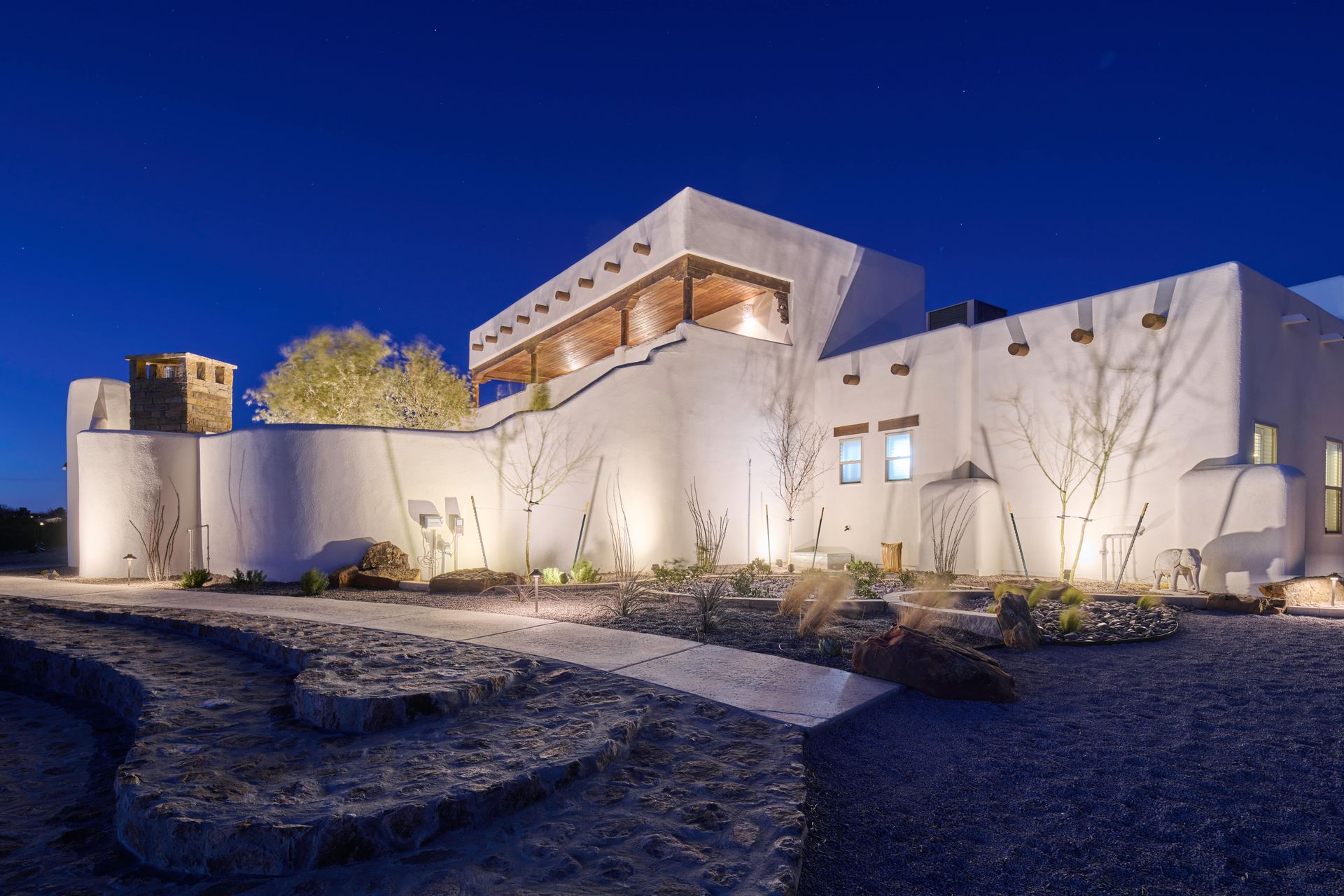 White stucco building with wooden accents at night, landscaped yard, blue sky.