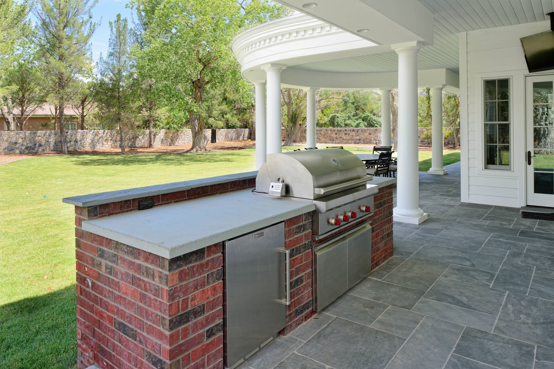 Outdoor kitchen with red brick base, stainless steel appliances, and gray countertop.