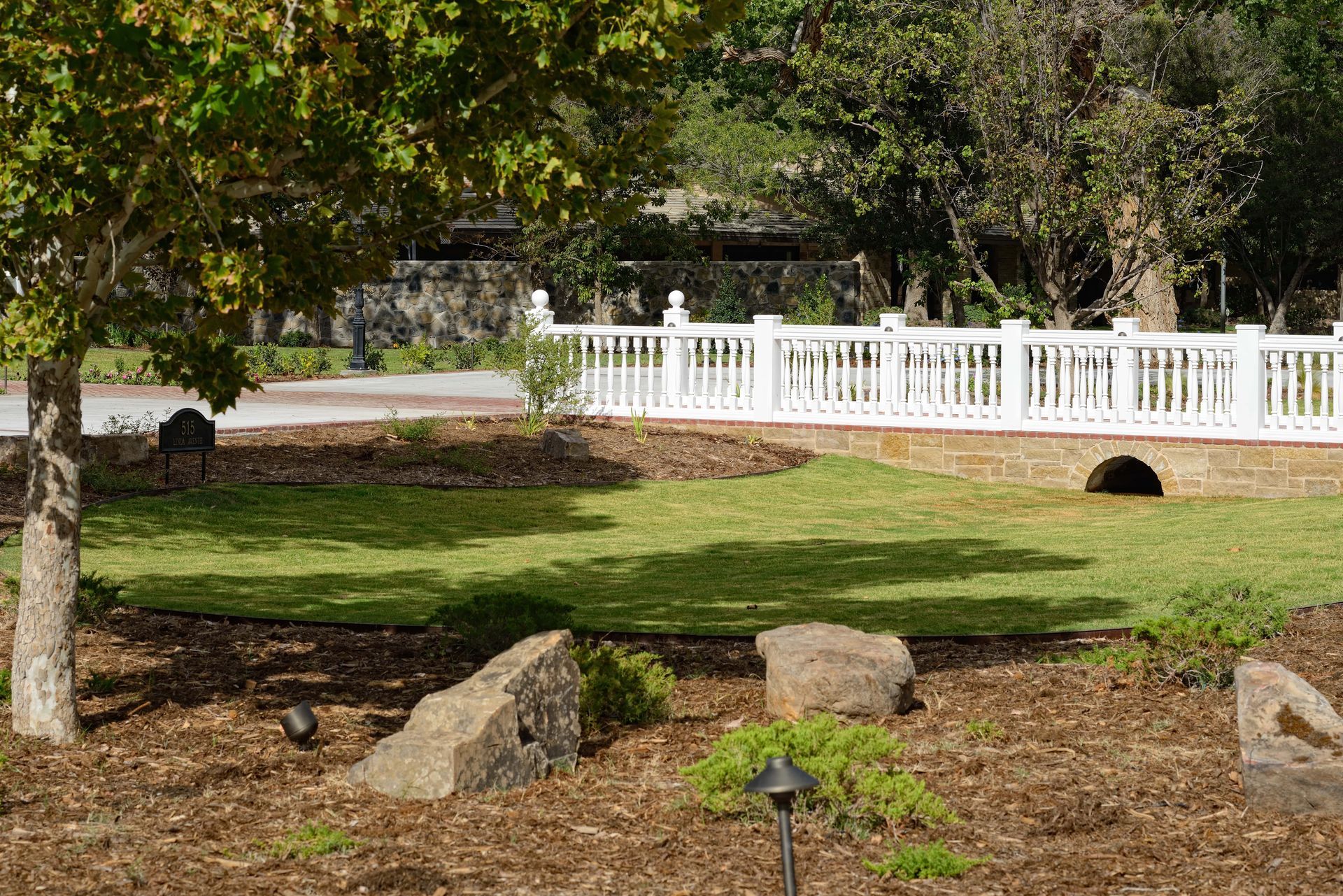 Park landscape with white fence, green grass, trees, and rocks.