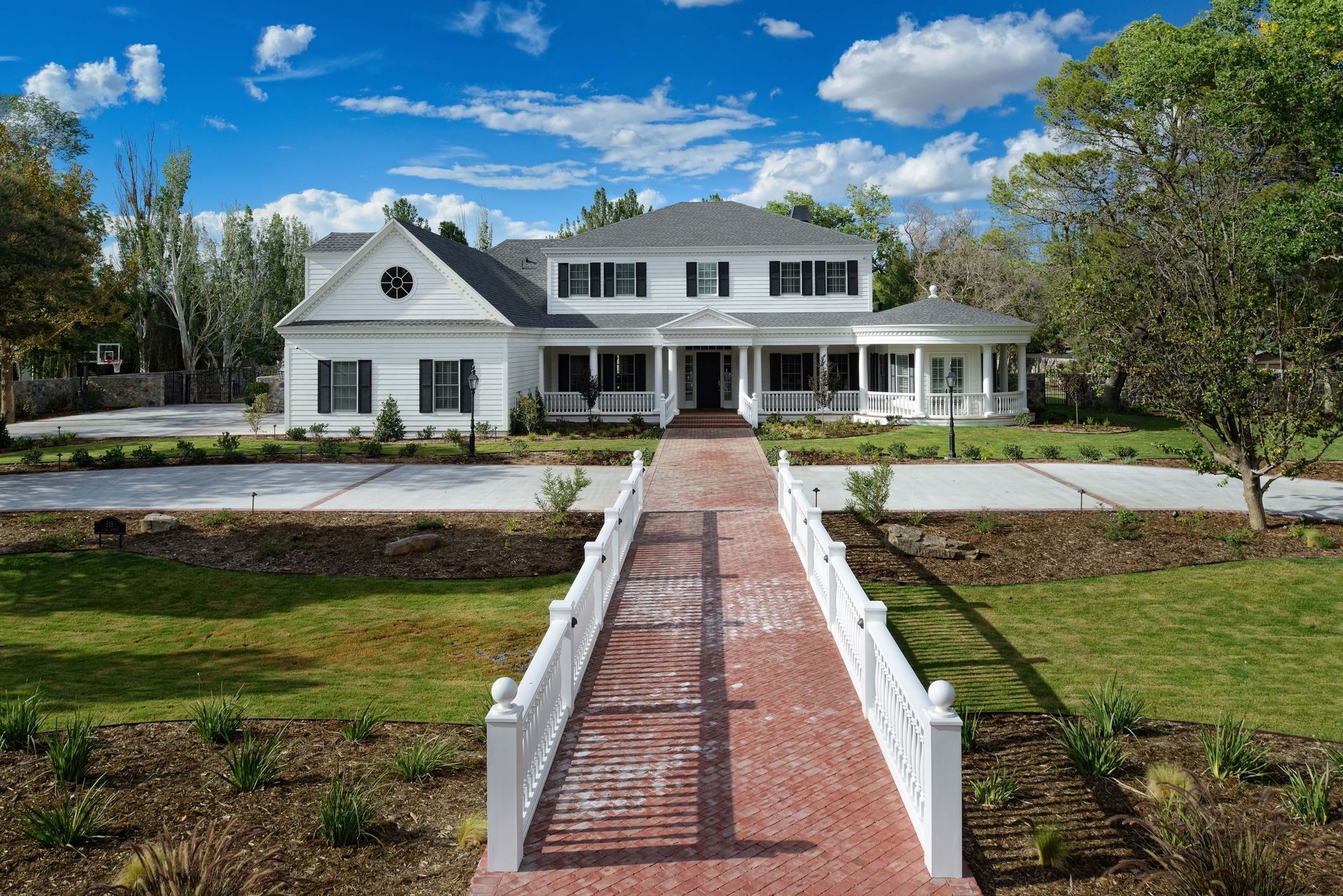 White two-story house with black shutters, red brick walkway, and a landscaped lawn.