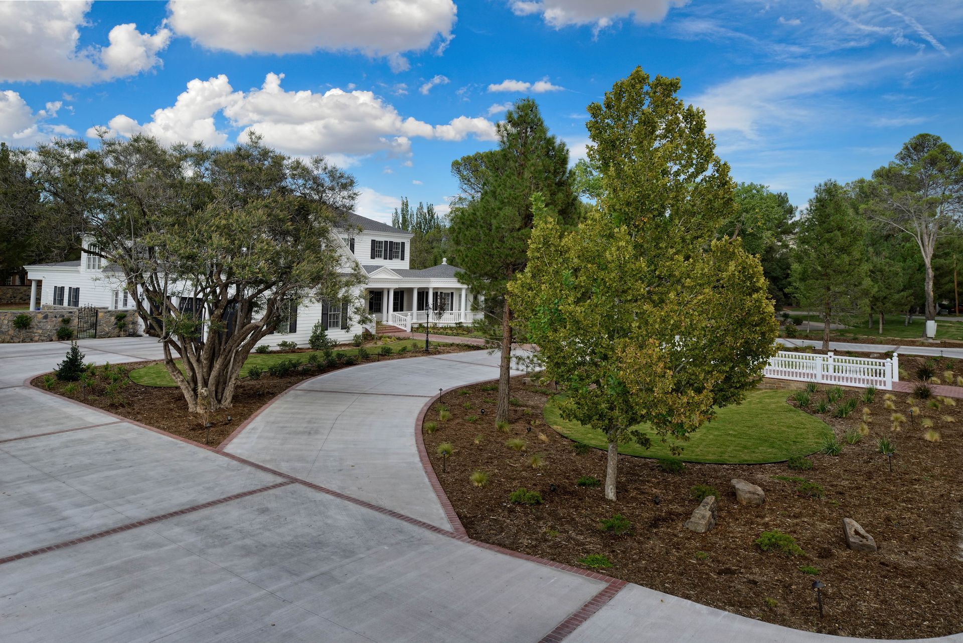 White house with a curved driveway and manicured landscaping under a blue sky.
