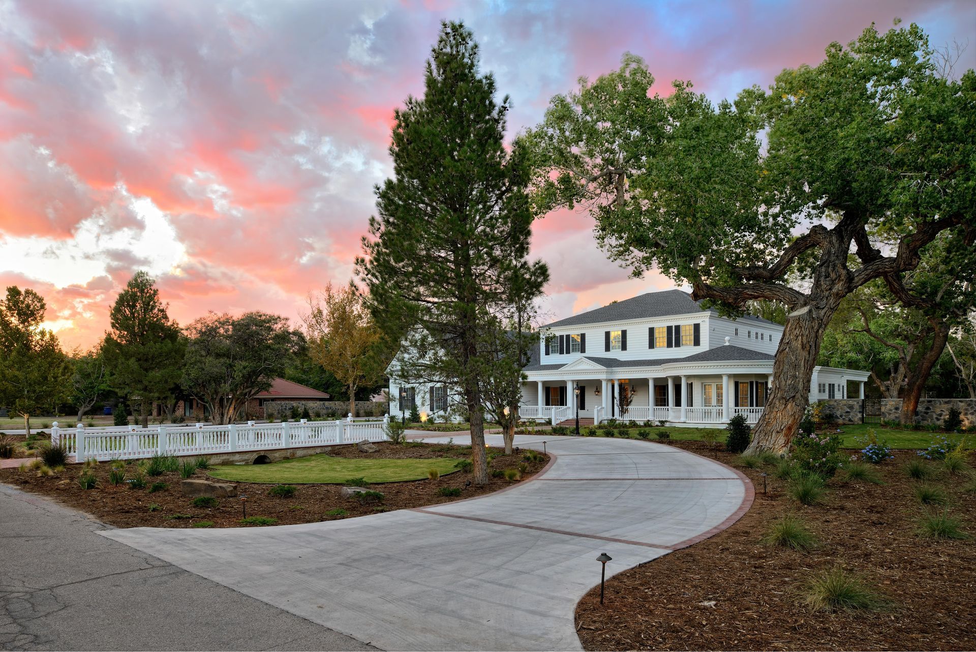 White mansion with a long driveway under a sunset sky.