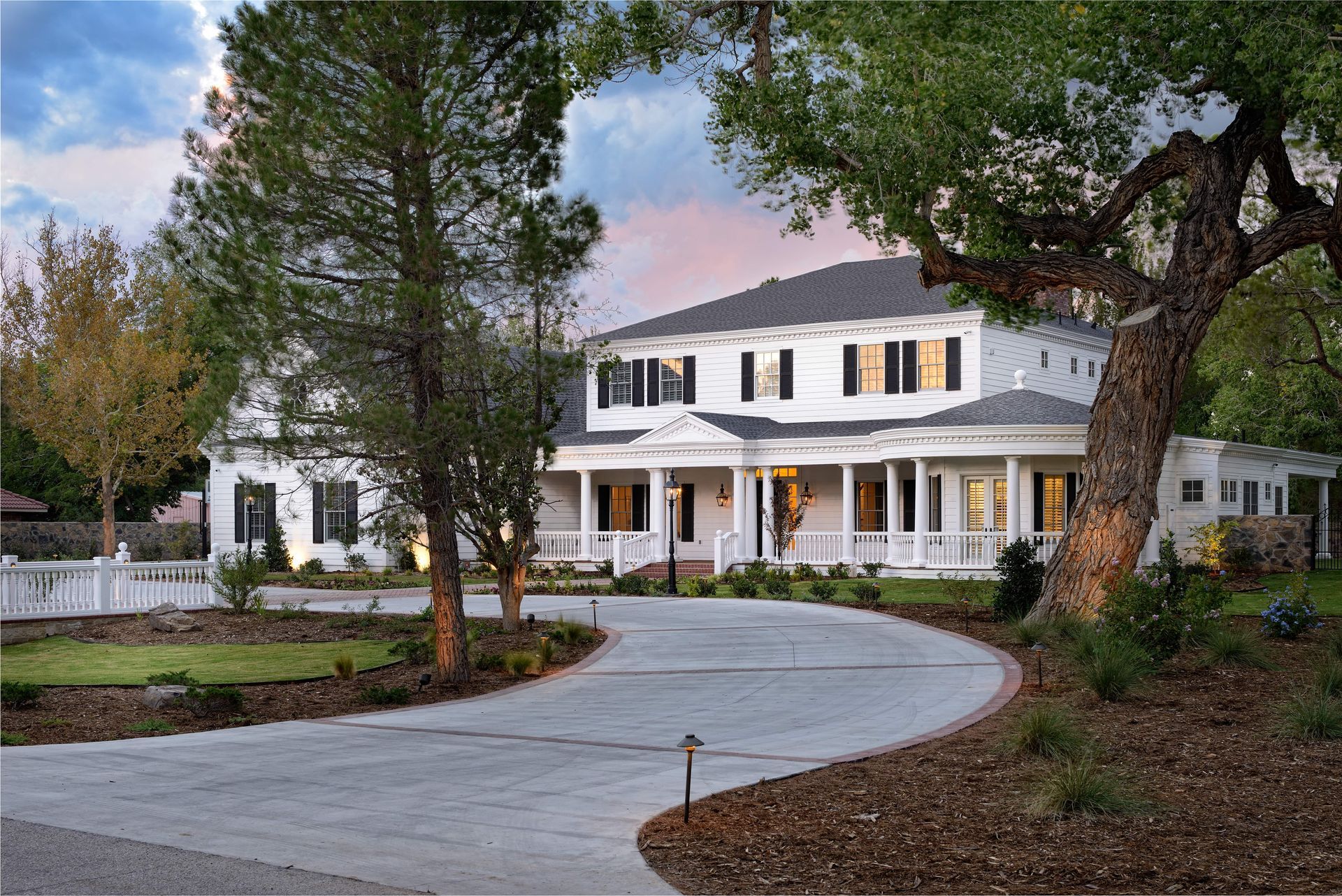 White house with a curved driveway, columns, and trees.