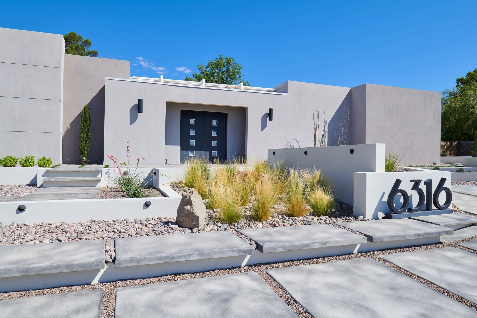 Modern home exterior with neutral stucco, concrete walkway, and desert landscaping.