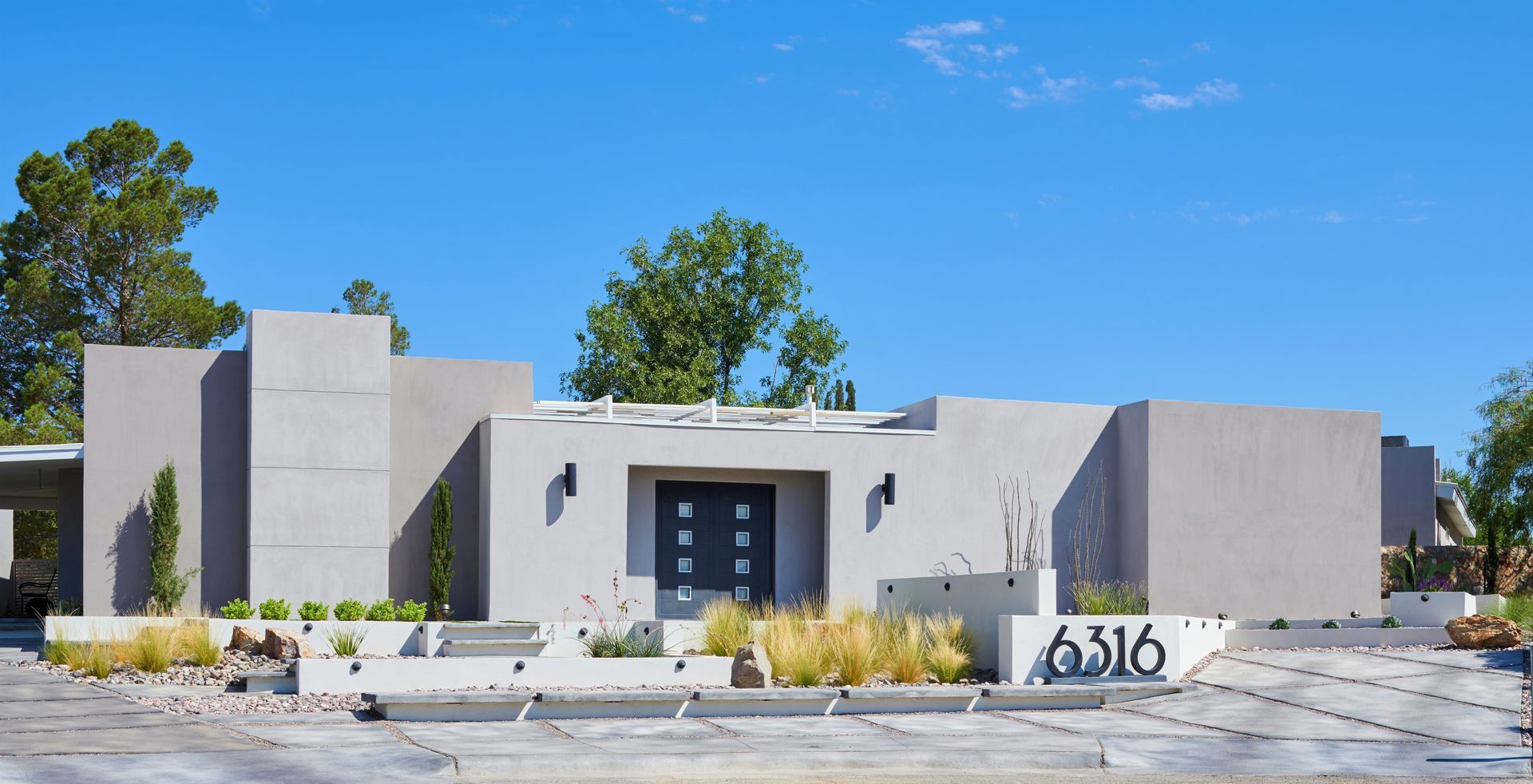 Modern, light gray stucco home with flat roof and blue sky. Address