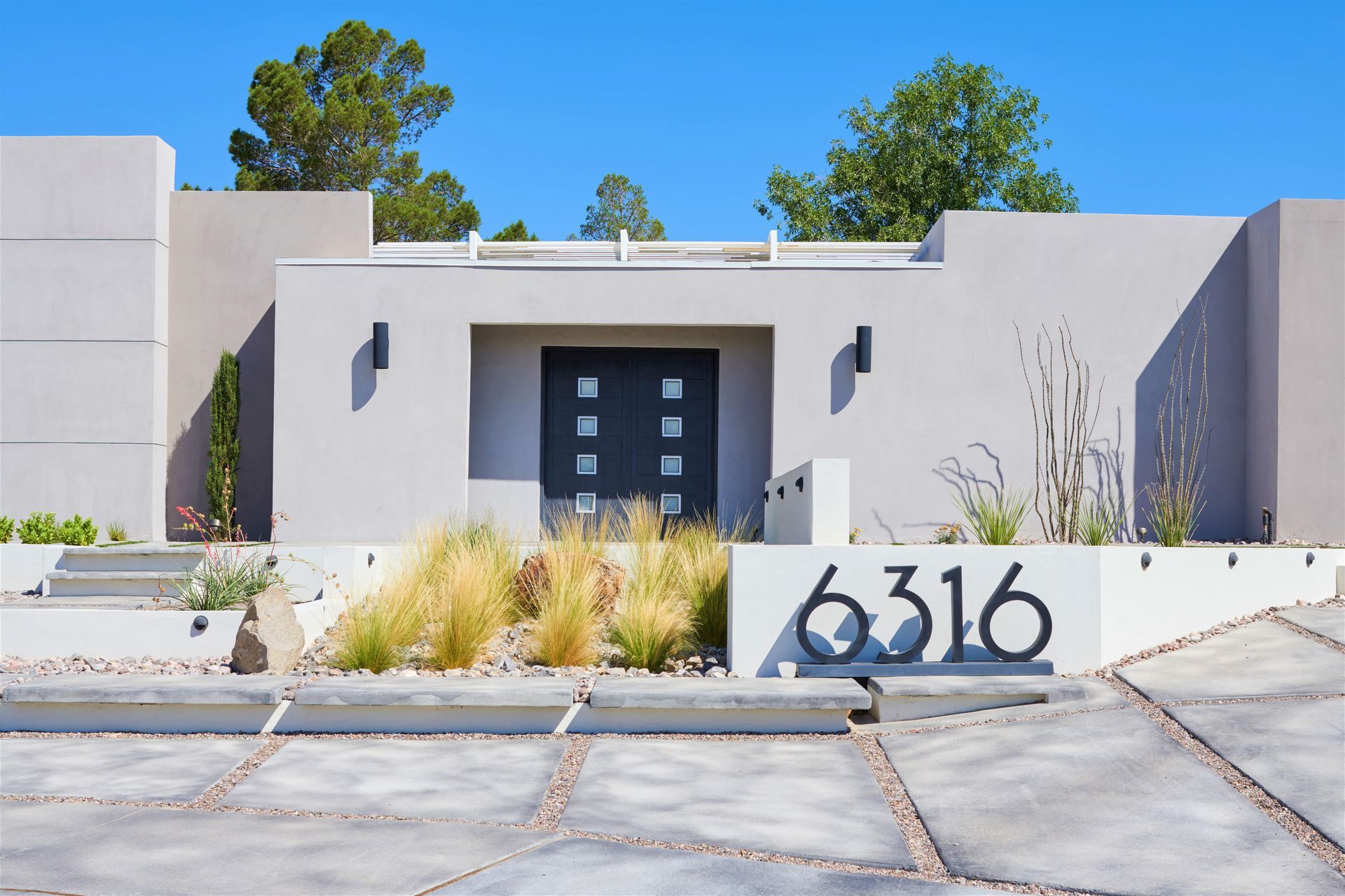 Modern home exterior with gray facade, blue door, and minimalist landscaping.