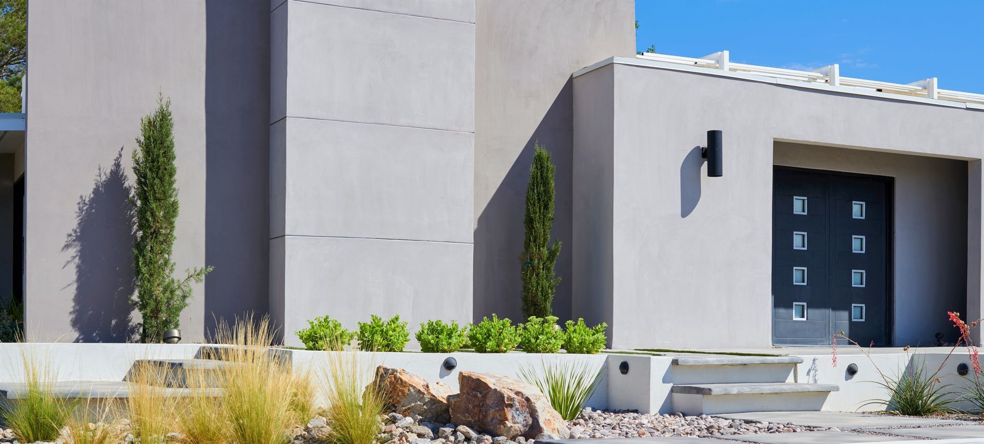 Modern house exterior with a gray facade, black door, and landscaping.