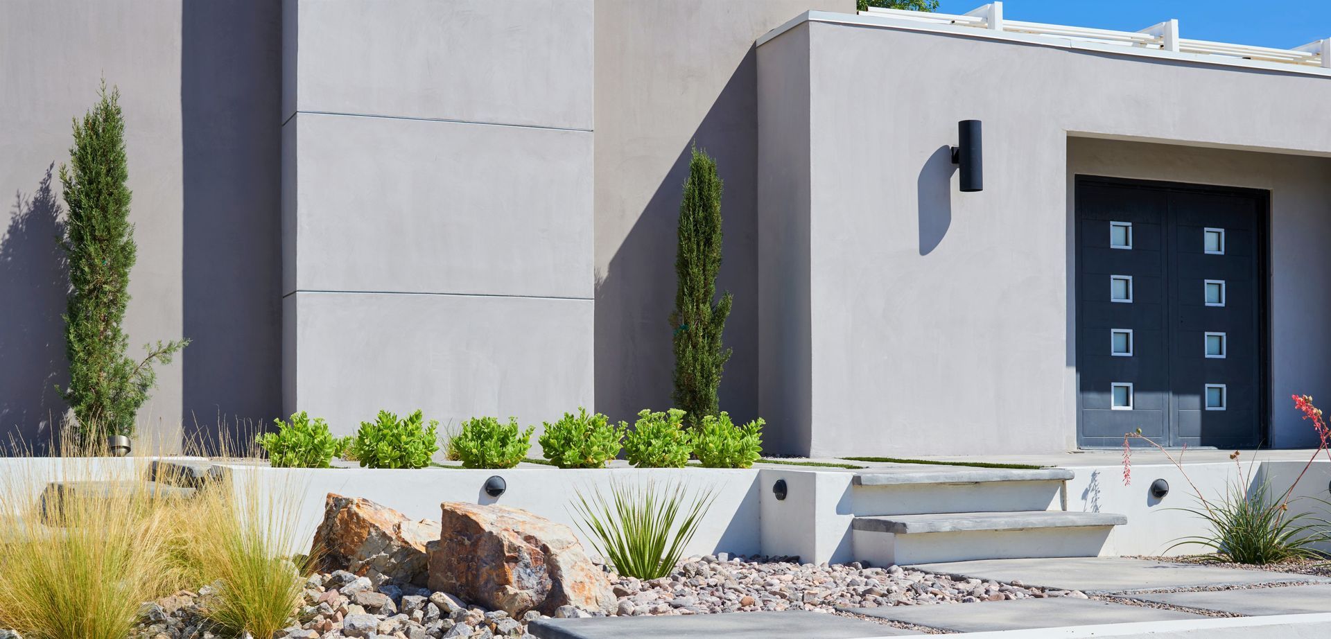 Modern house exterior with gray walls, front door, and manicured landscaping.
