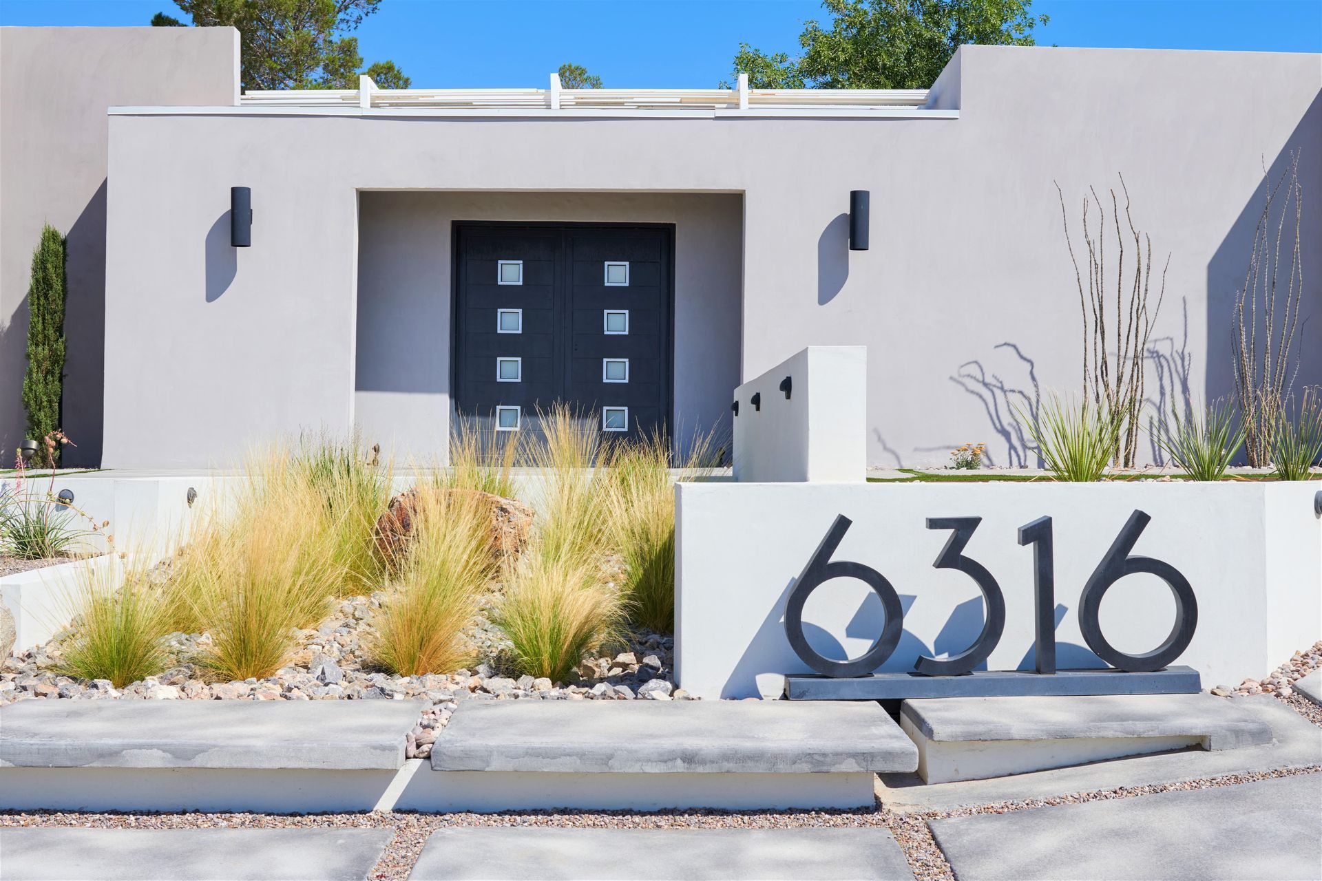 Modern house exterior with gray stucco, dark front door, and large address numbers.